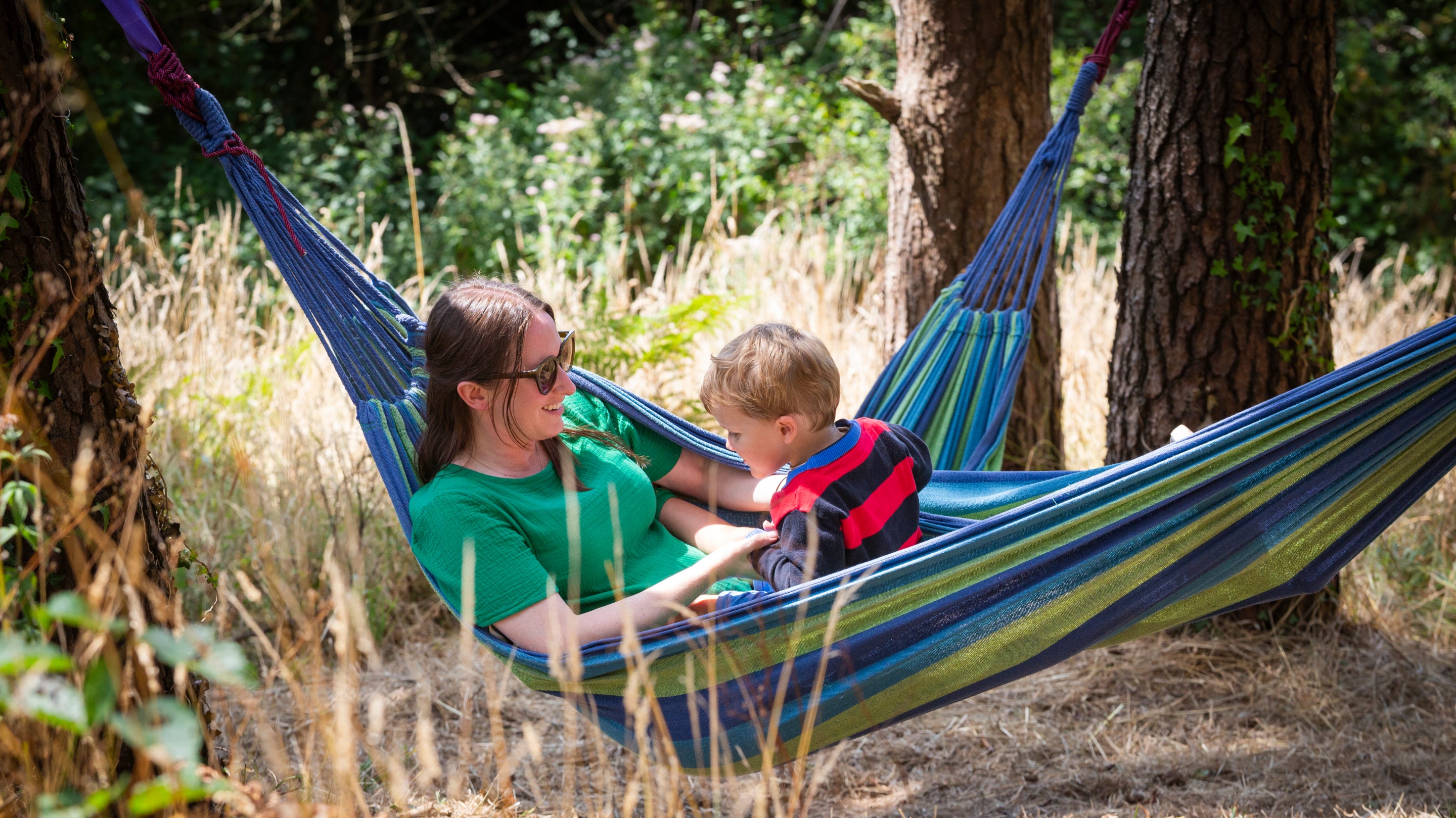 A family relax in hammocks in woodland at Coleton Fishacre, Devon
