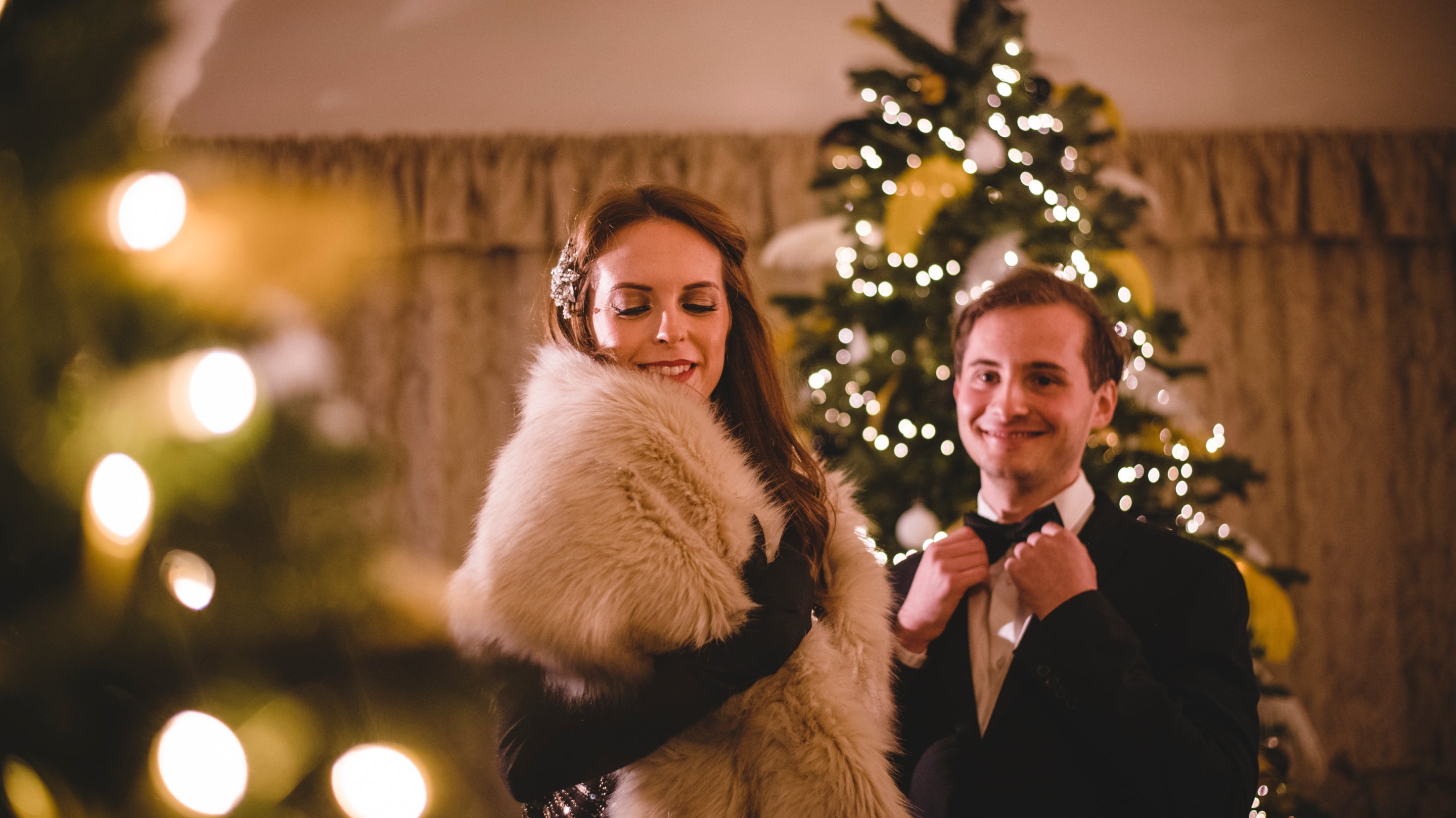 Two people dressed in 1920s clothing pose by a gold and white Christmas tree.