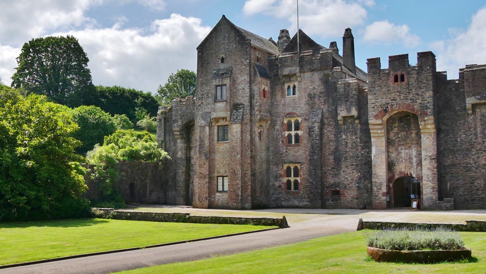 Stone fortified walls in front of two grass lawns with a gravel drive