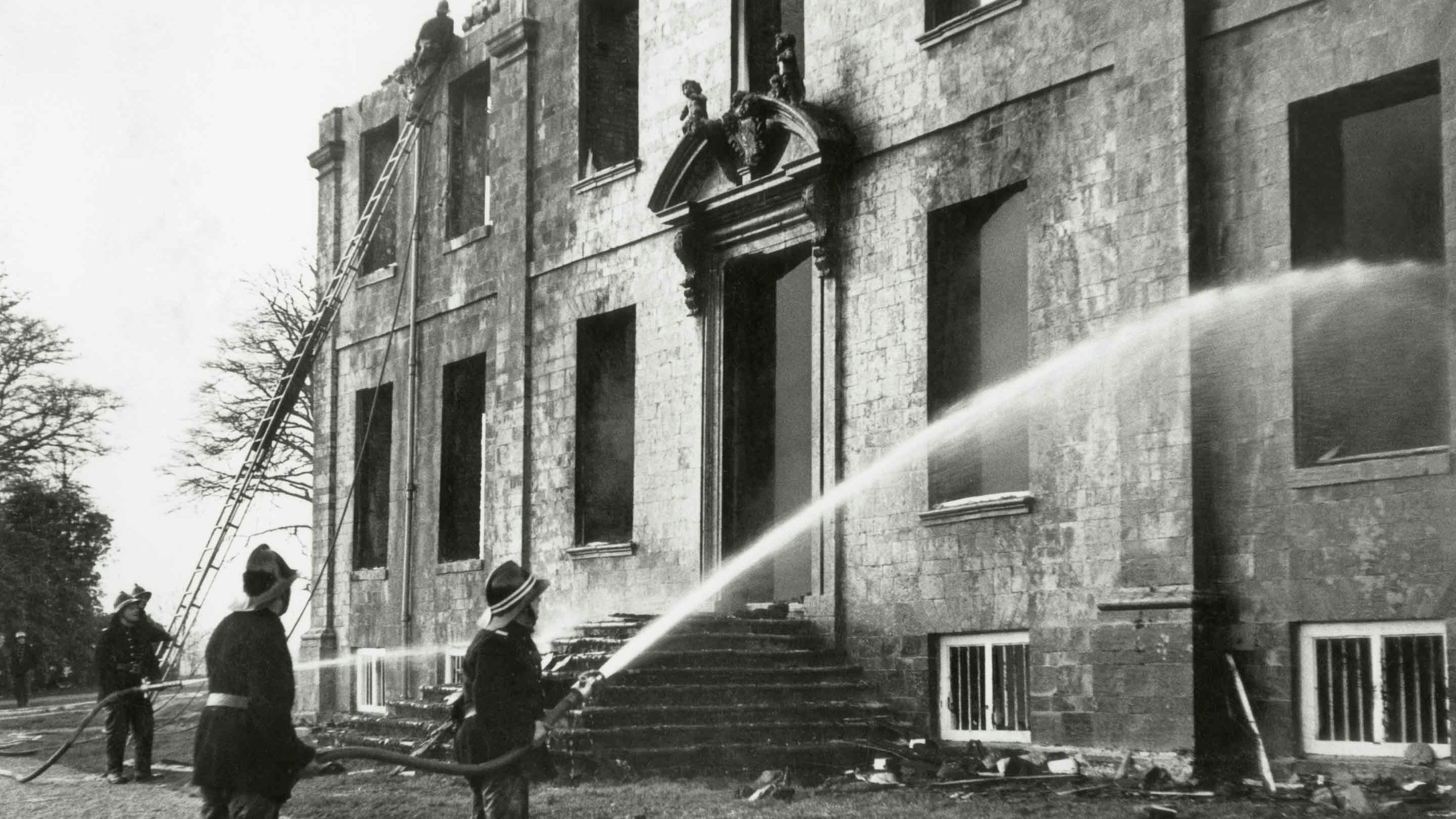 Three firemen extinguishing fire at the gutted north front of Dunsland