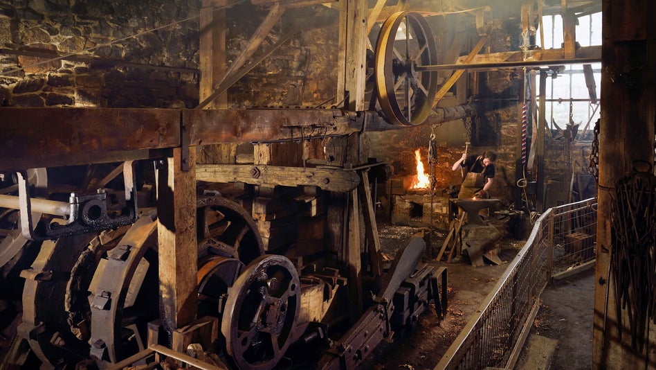 Blacksmith working in the water-powered forge at Finch Foundry, Devon