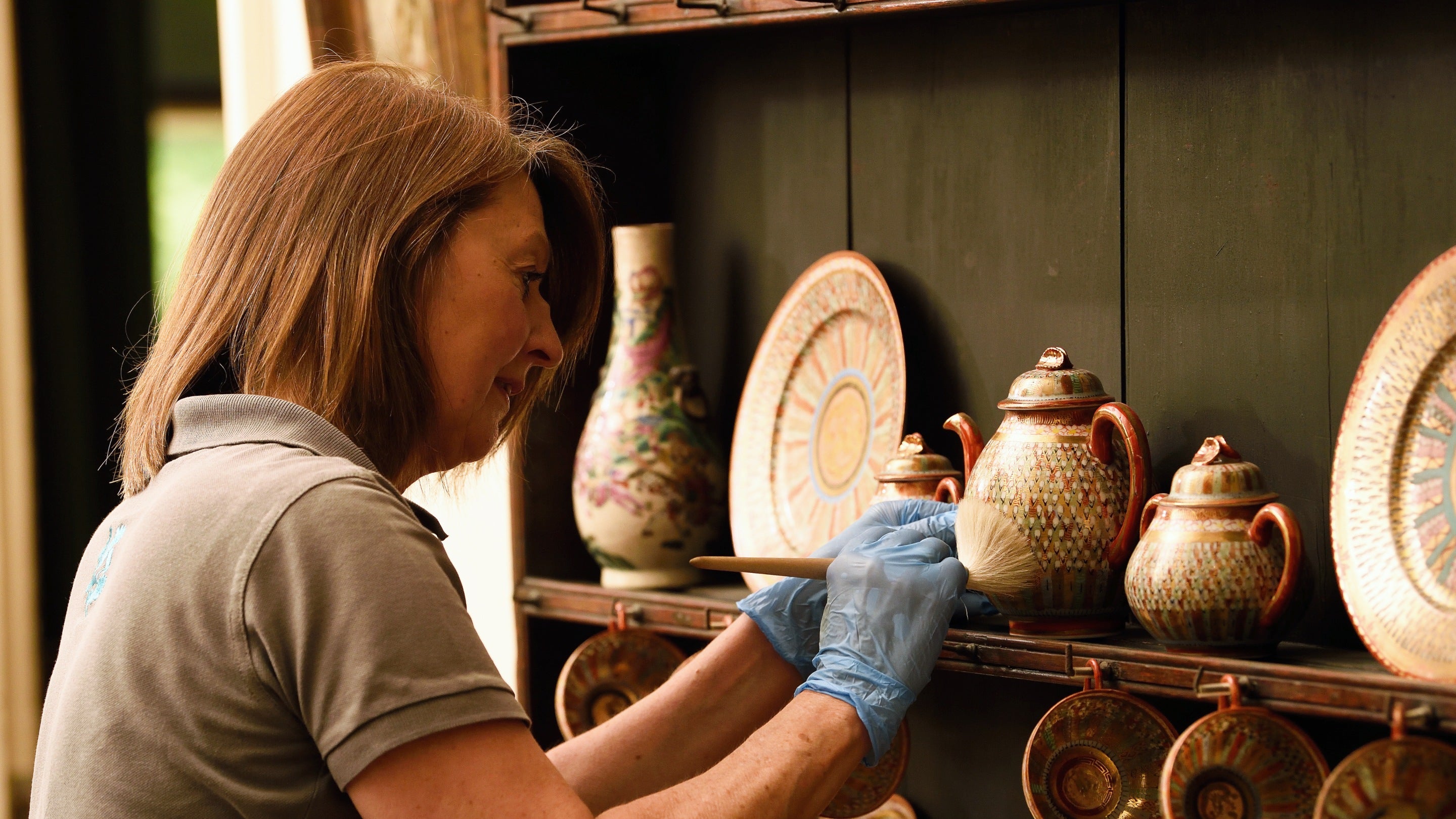 A conservation assistant carefully dusting objects on the shelves at Greenway, Devon
