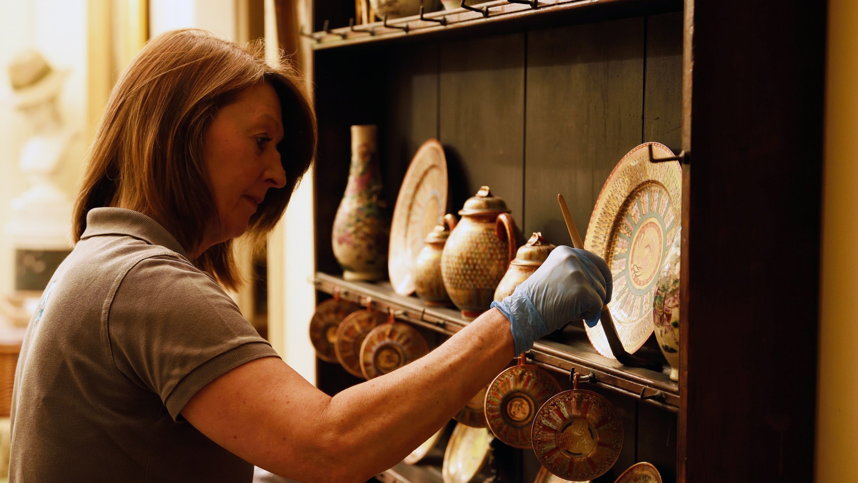 A conservation assistant carefully dusts objects at Greenway, Devon