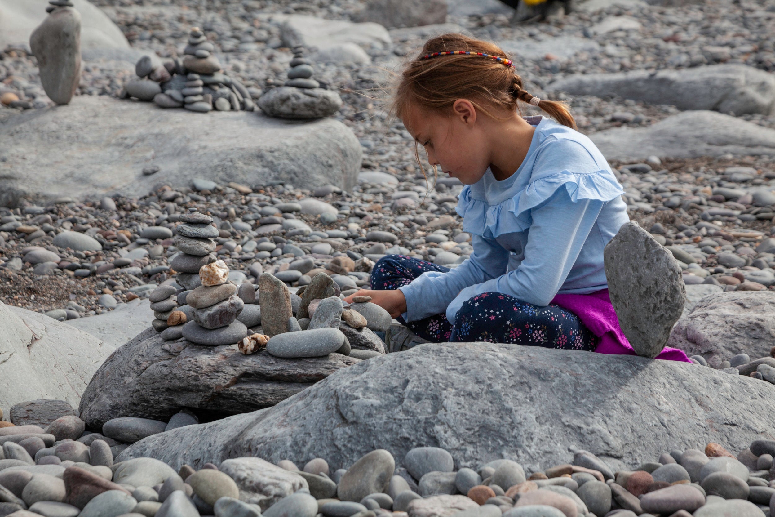 A young girl practices stone balancing on the beach at Heddon Valley, Devon