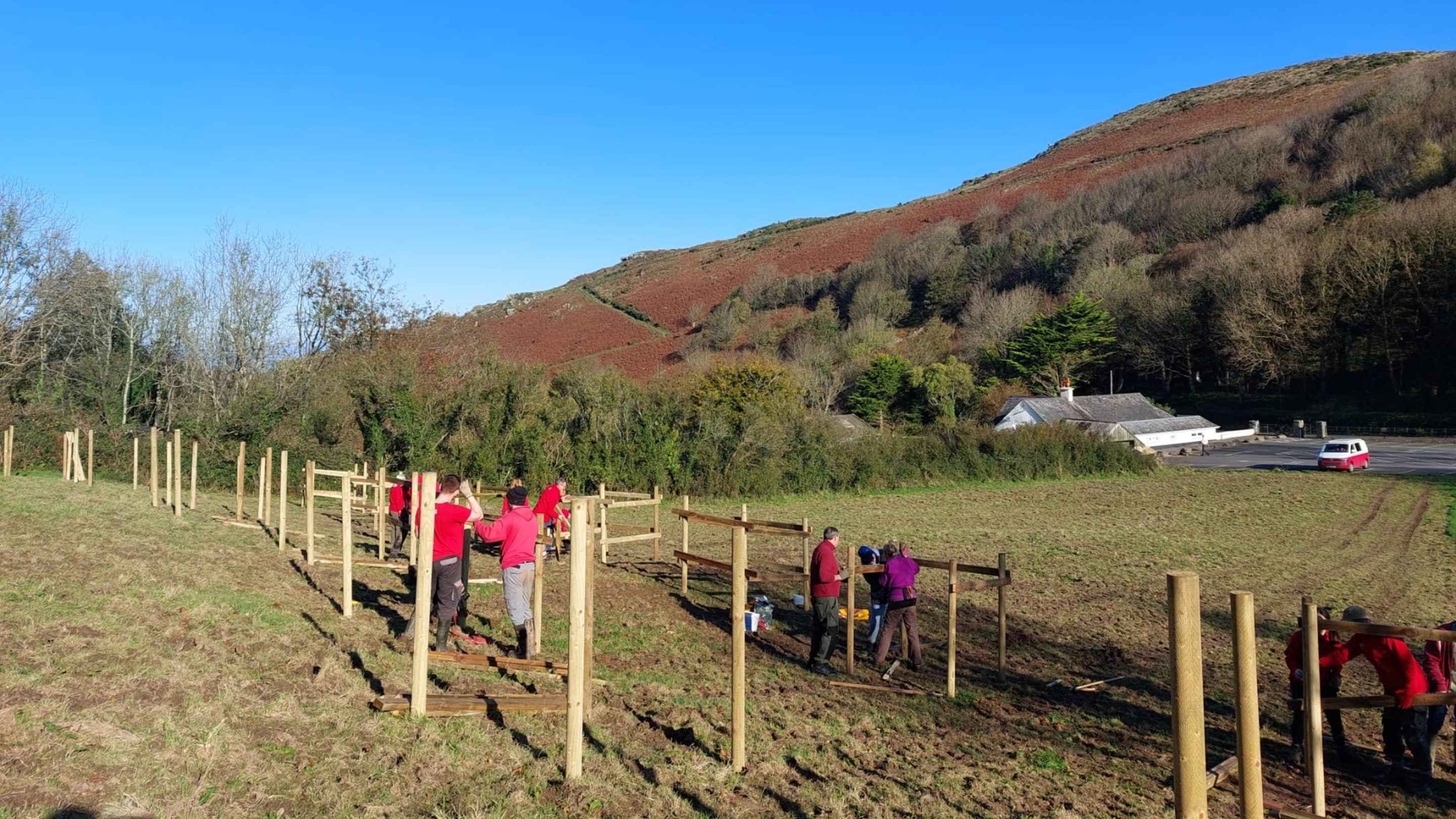 Volunteers building fences to protect an orchard with view of rocky hills behind.