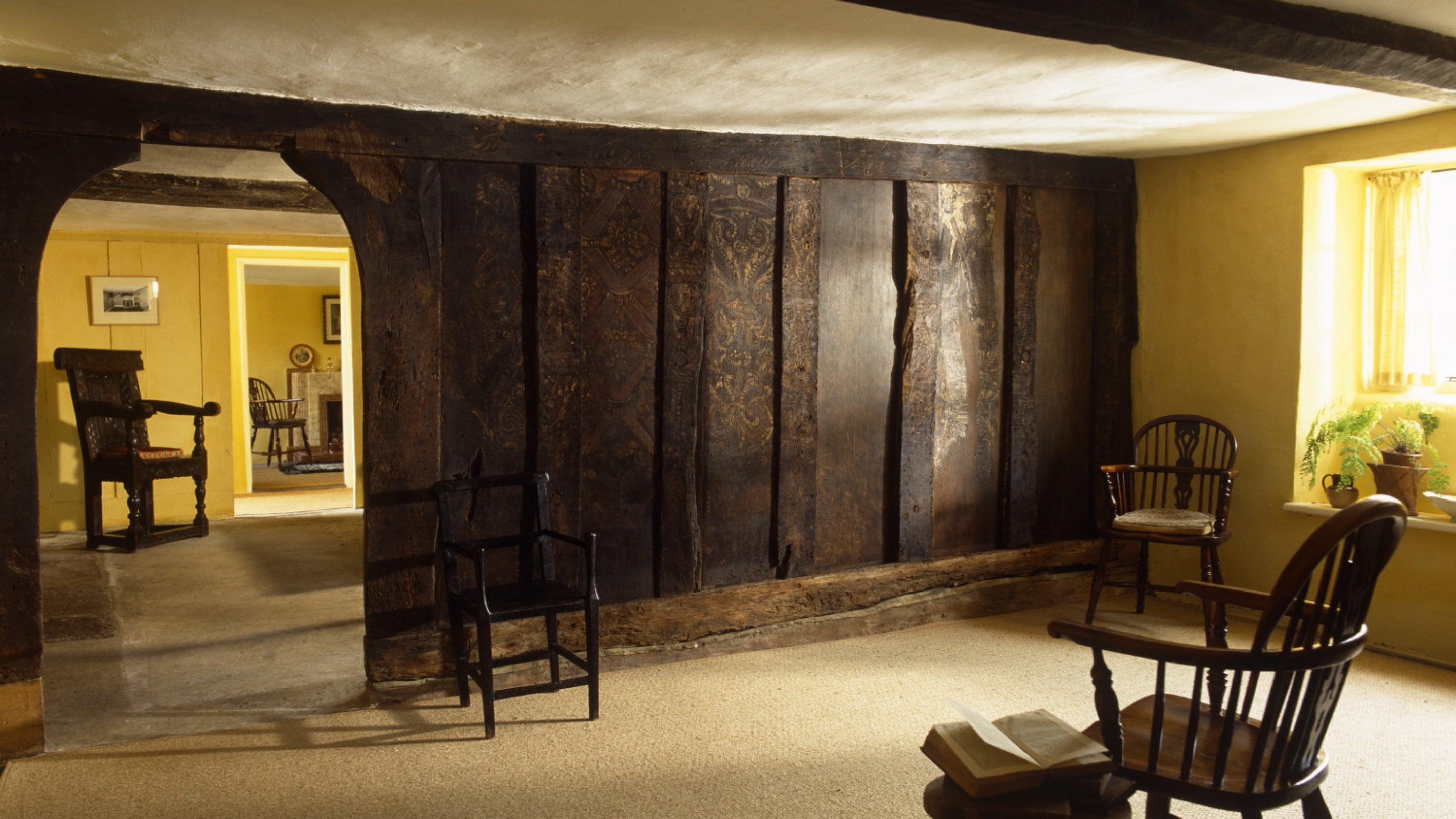 A view of the Parlour at Marker's Cottage on the Killerton Estate, with a large painted wooden screen across one wall and a glimpse into the yellow-painted hall.