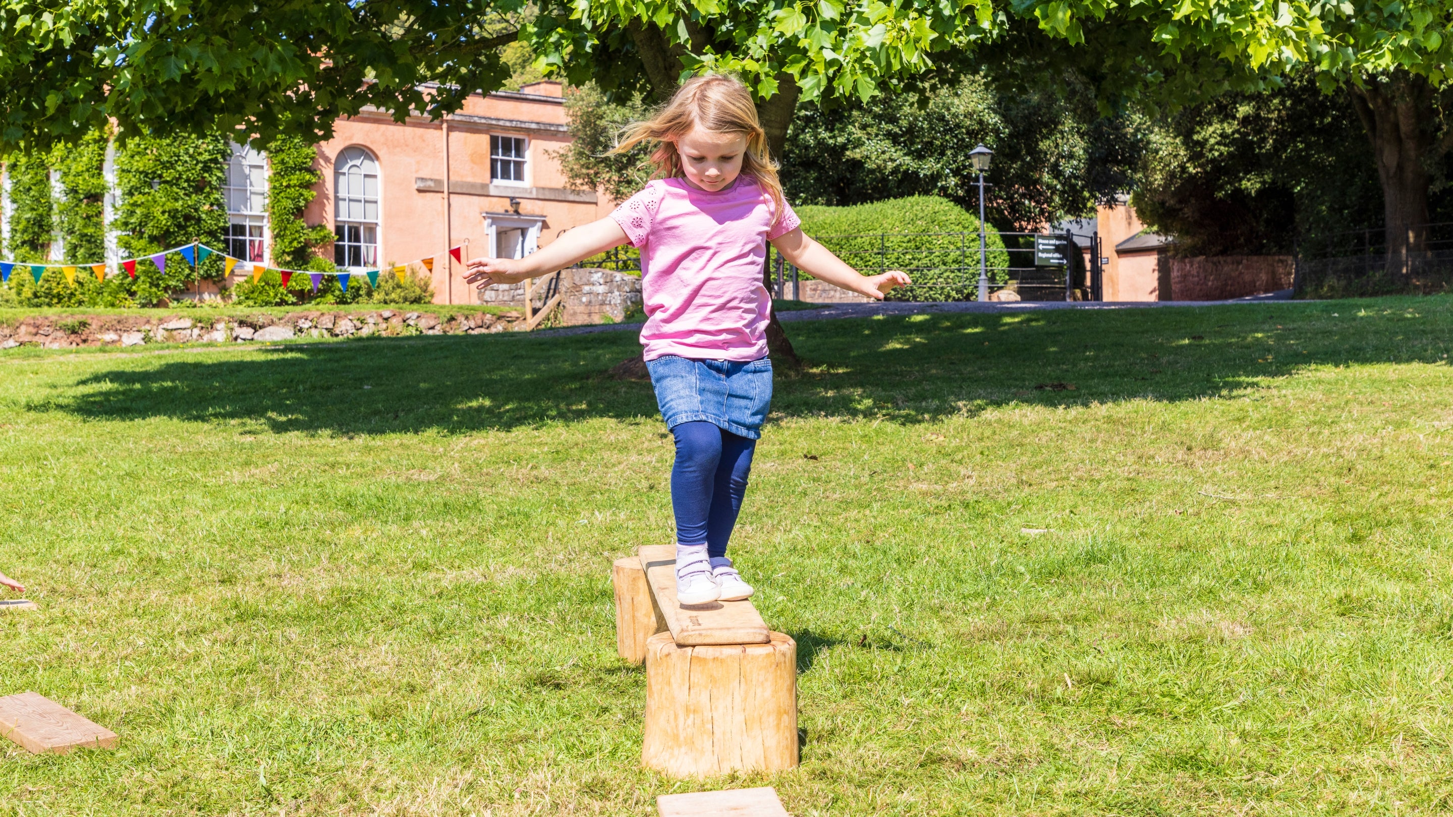 Small child balancing on a beam in front of Killerton House