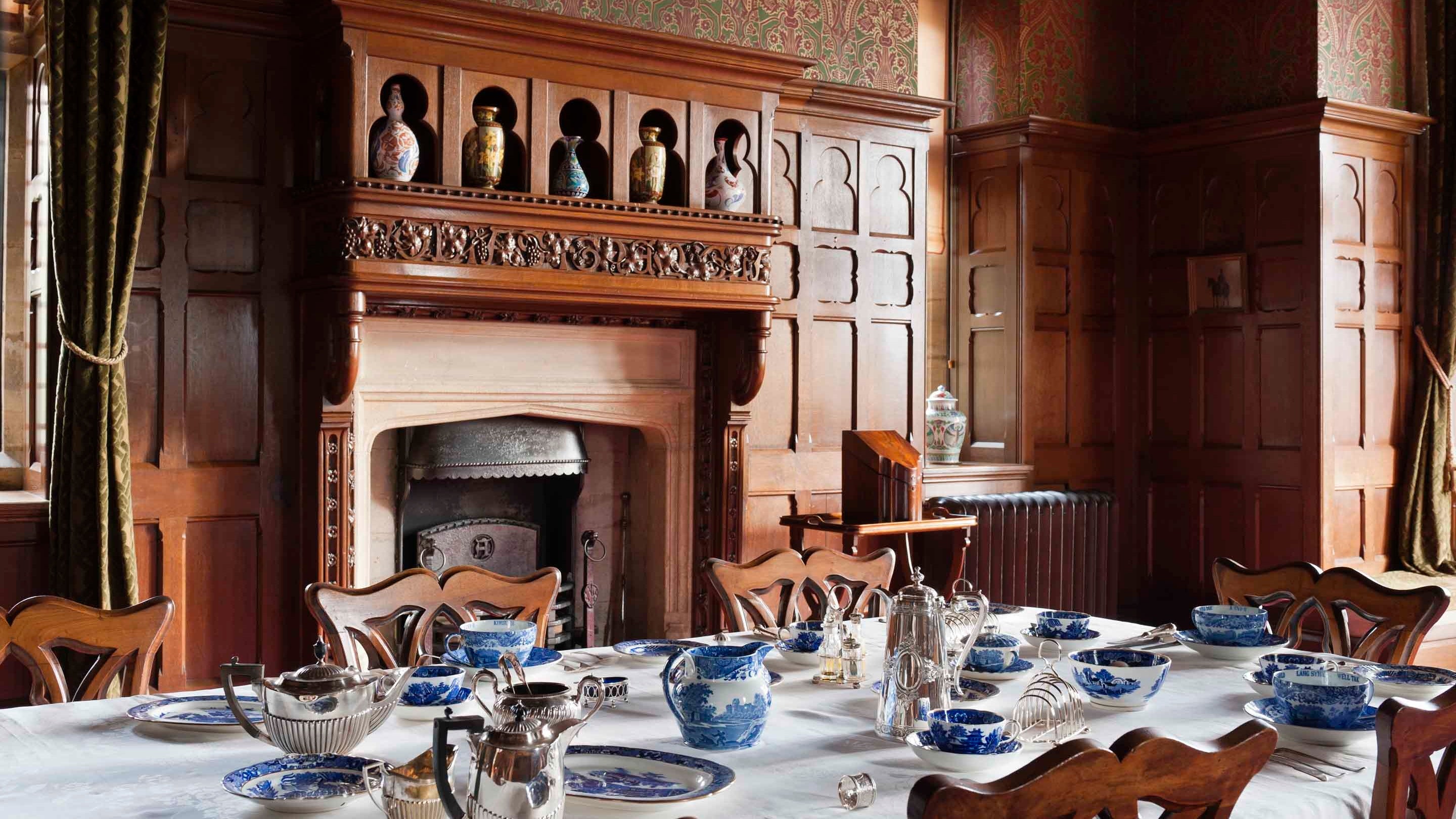 A view of the dining room at Knightshayes Court with a huge wooden fireplace surrounded by panelling and blue and white china on the table in front of it