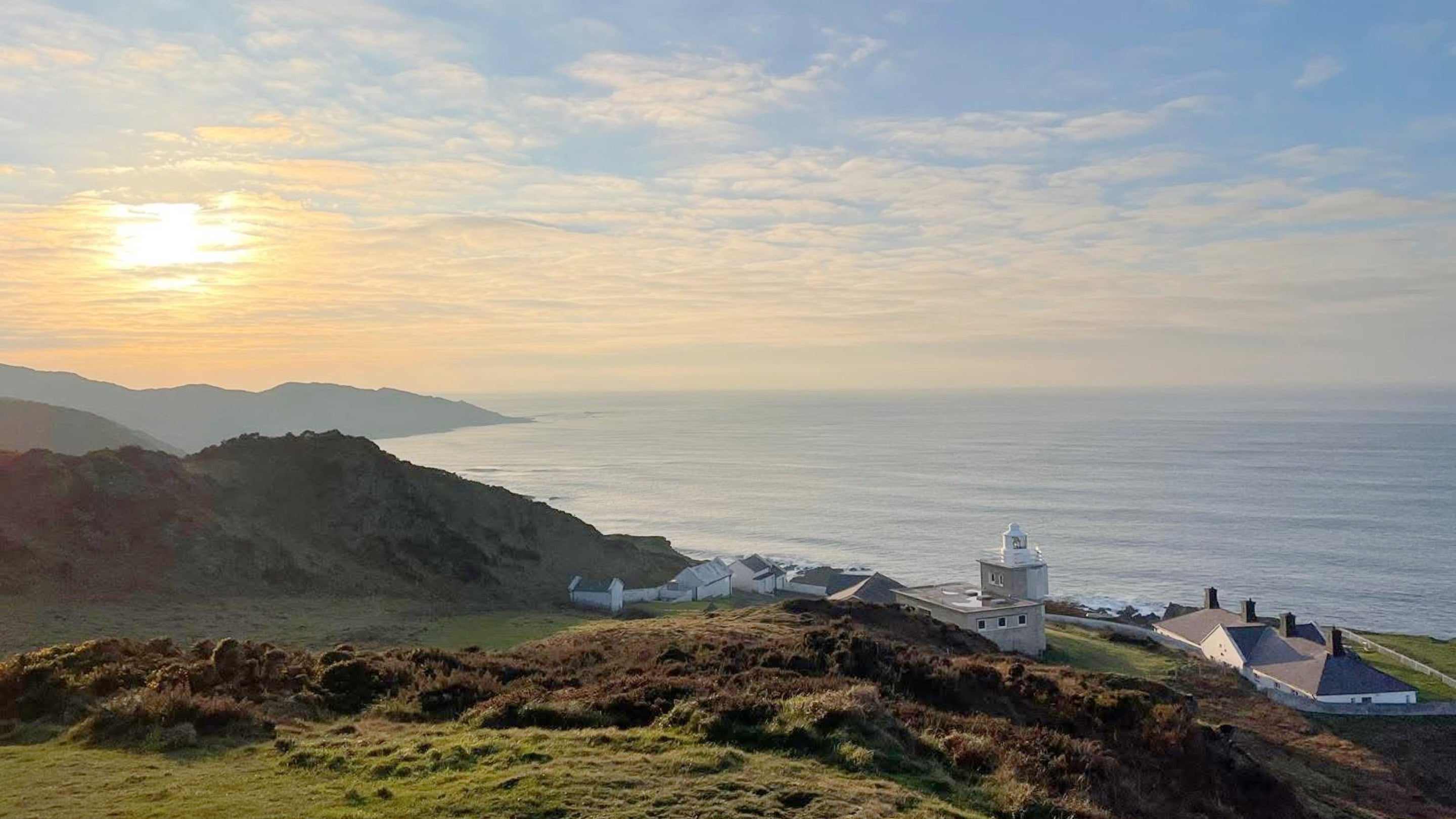 Sunset over the sea with a light house on a cliff in the foreground