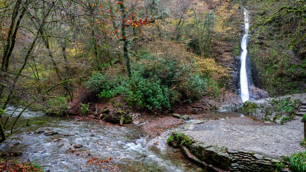The white cascade of Whitelady Waterfall flows down the rock with trees around turning autumn colours of orange, gold and brown.