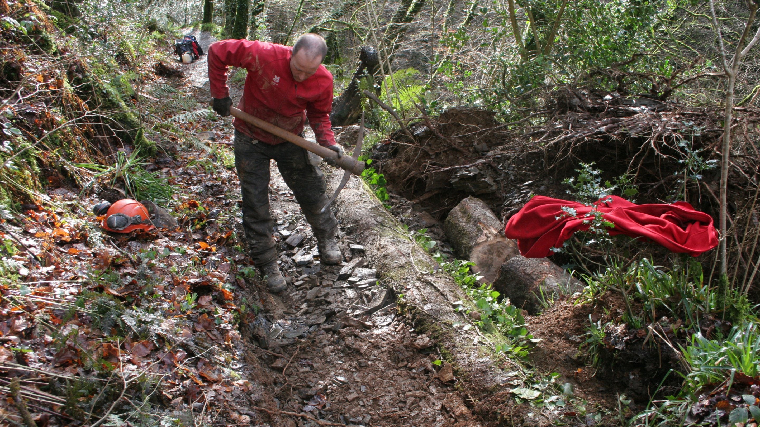 Ranger in red top working with a pick axe to repair a path at Lydford Gorge