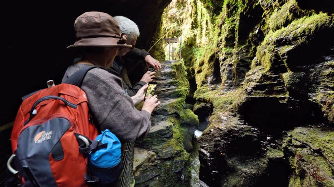 Visitors taking photos with mobile phones on the viewing platform of the Devil's Cauldron at Lydford Gorge, Devon