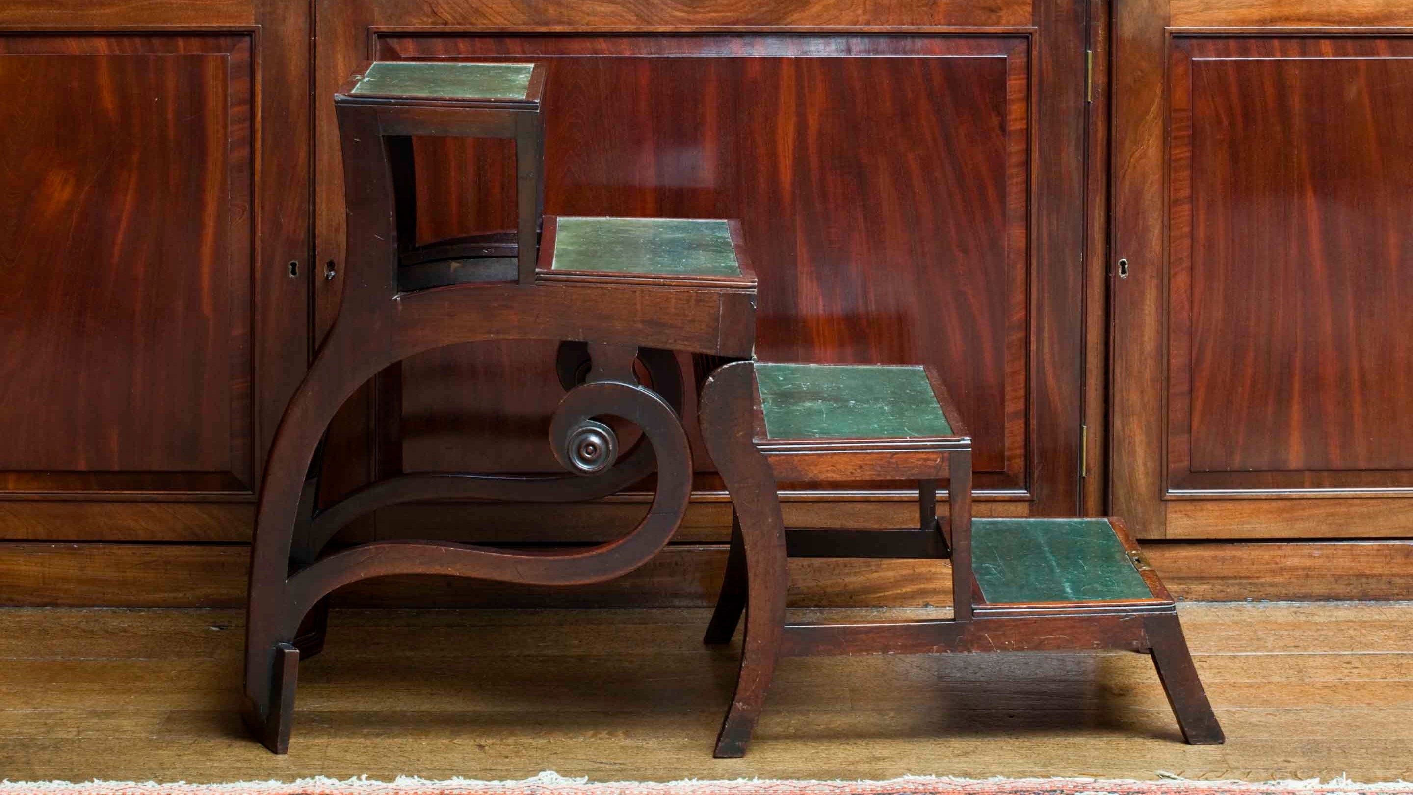 The 'Patent Metamorphic Library Chair' by Morgan and Sanders - a Regency mahogany library steps which can be folded to form a sabre-leg armchair, in the library at Saltram, Devon