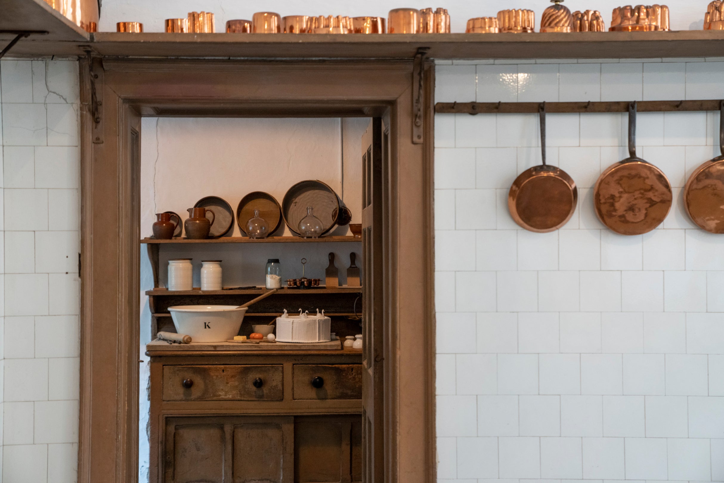 A view of Saltram's pantry with copper pans and mixing bowls through the door of the Kitchen