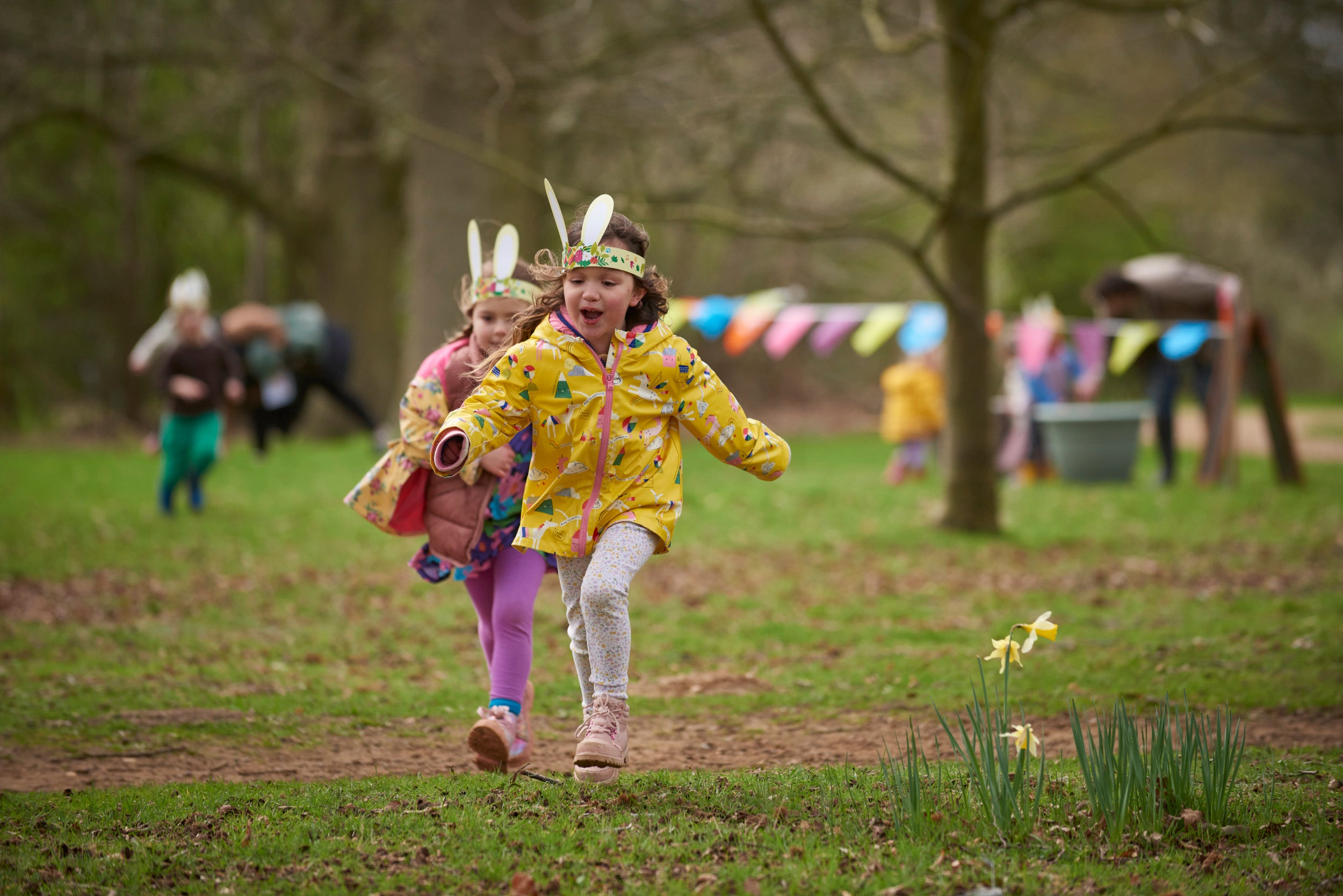 Two young girls wearing bunny ears run towards the camera laughing while enjoying an Easter trail