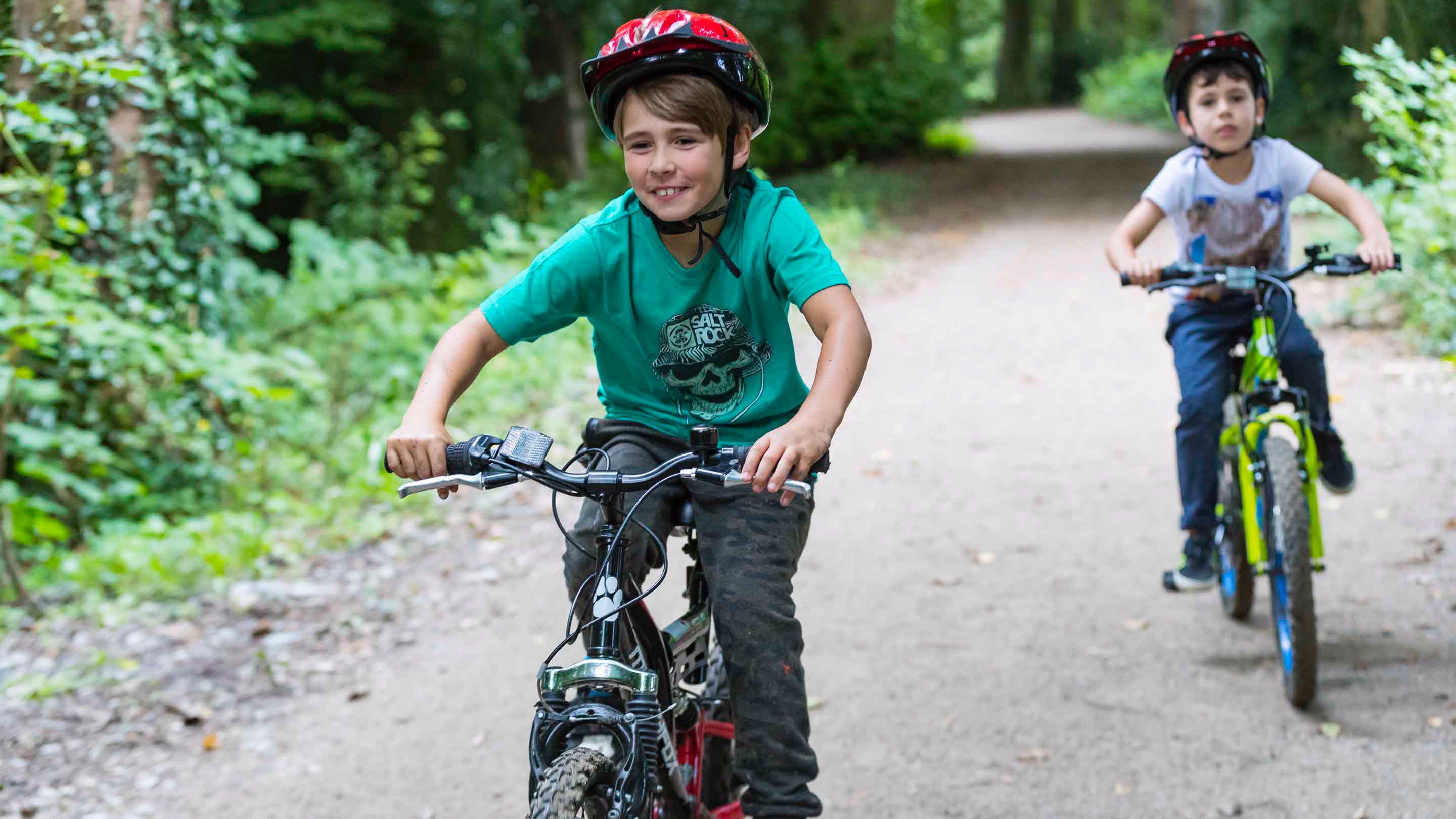 Two children ride bikes along a track through the woods at Saltram, Devon