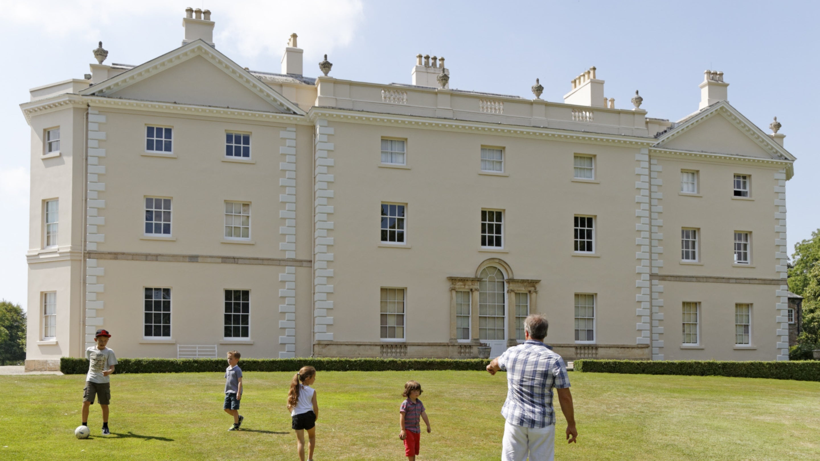 Family playing football on the grass in front of the house at Saltram