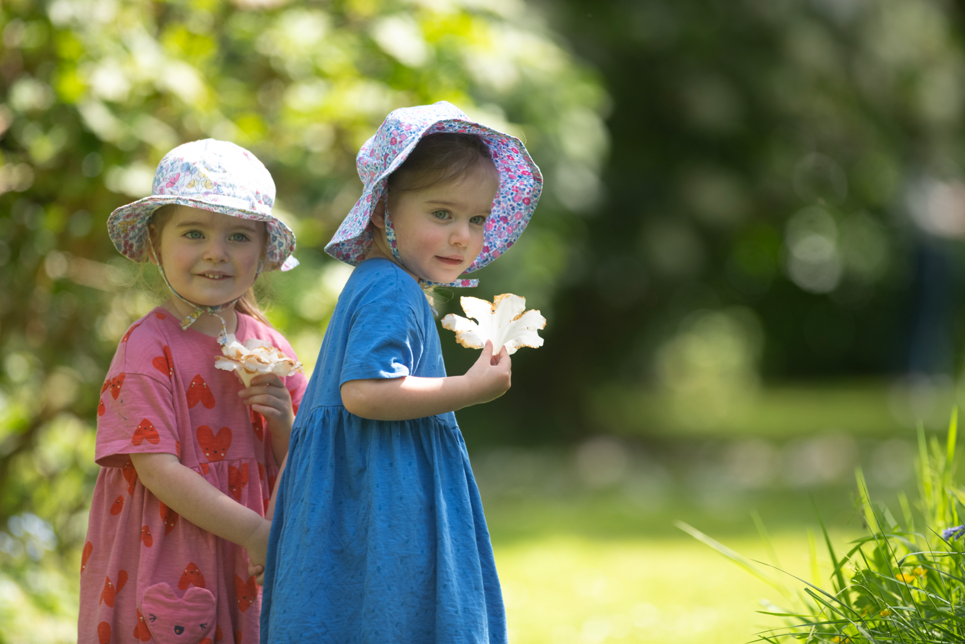 Two little twin in floral dresses hold a flower in the spring sunshine at Saltram
