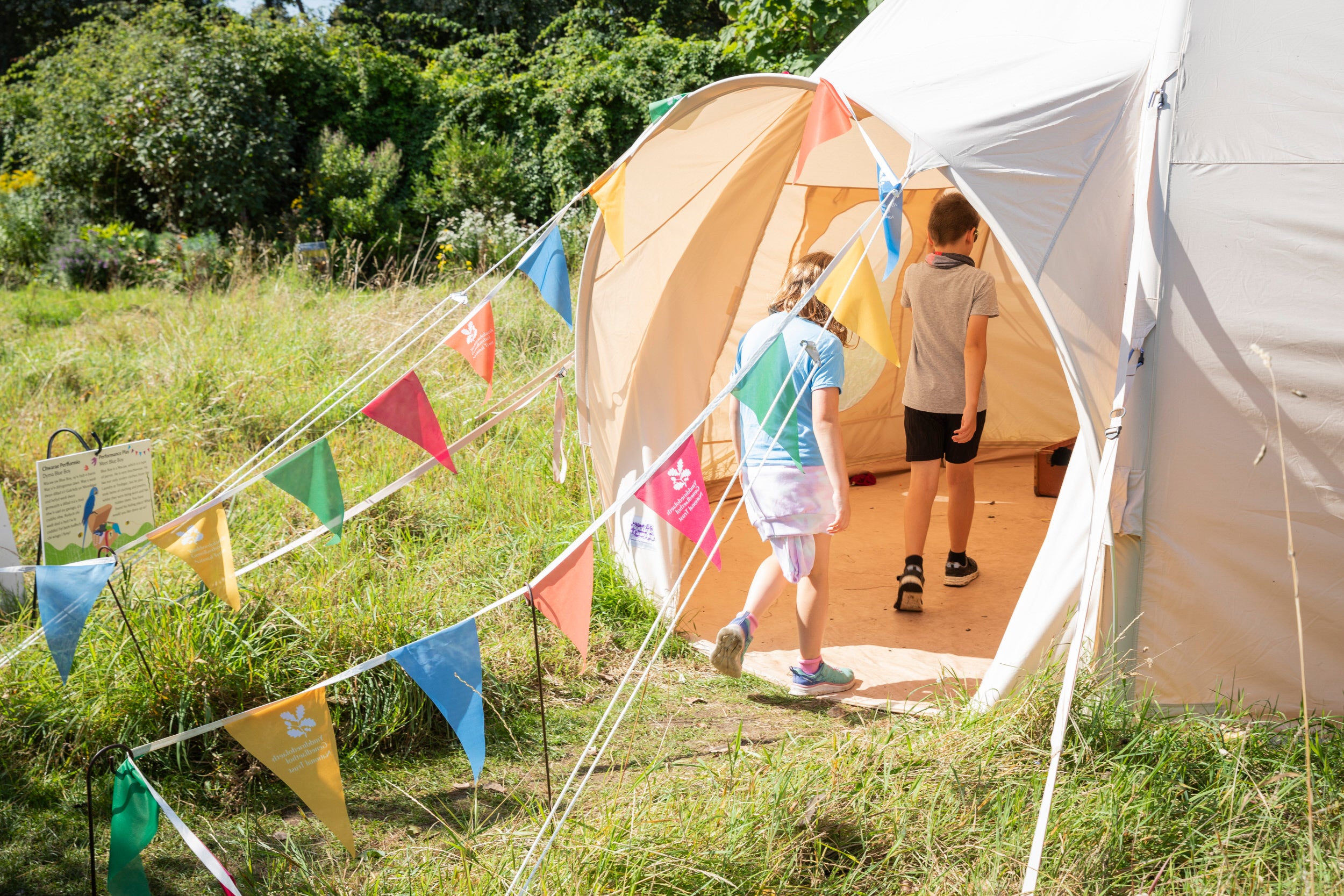 Two children walk into a play tent which has bunting