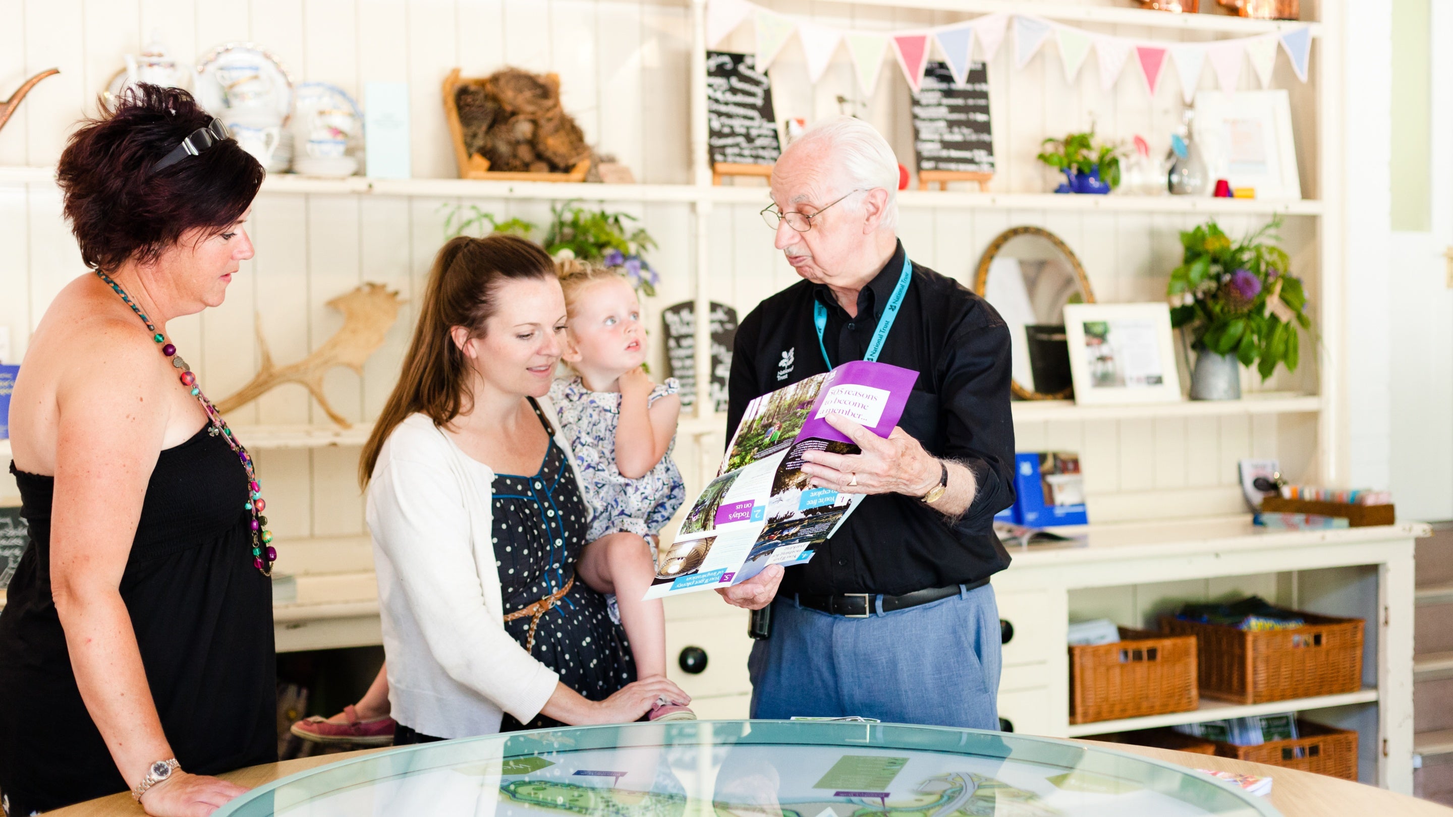 Visitors with a child talk to a volunteer inside the Welcome Centre at Saltram, Devon