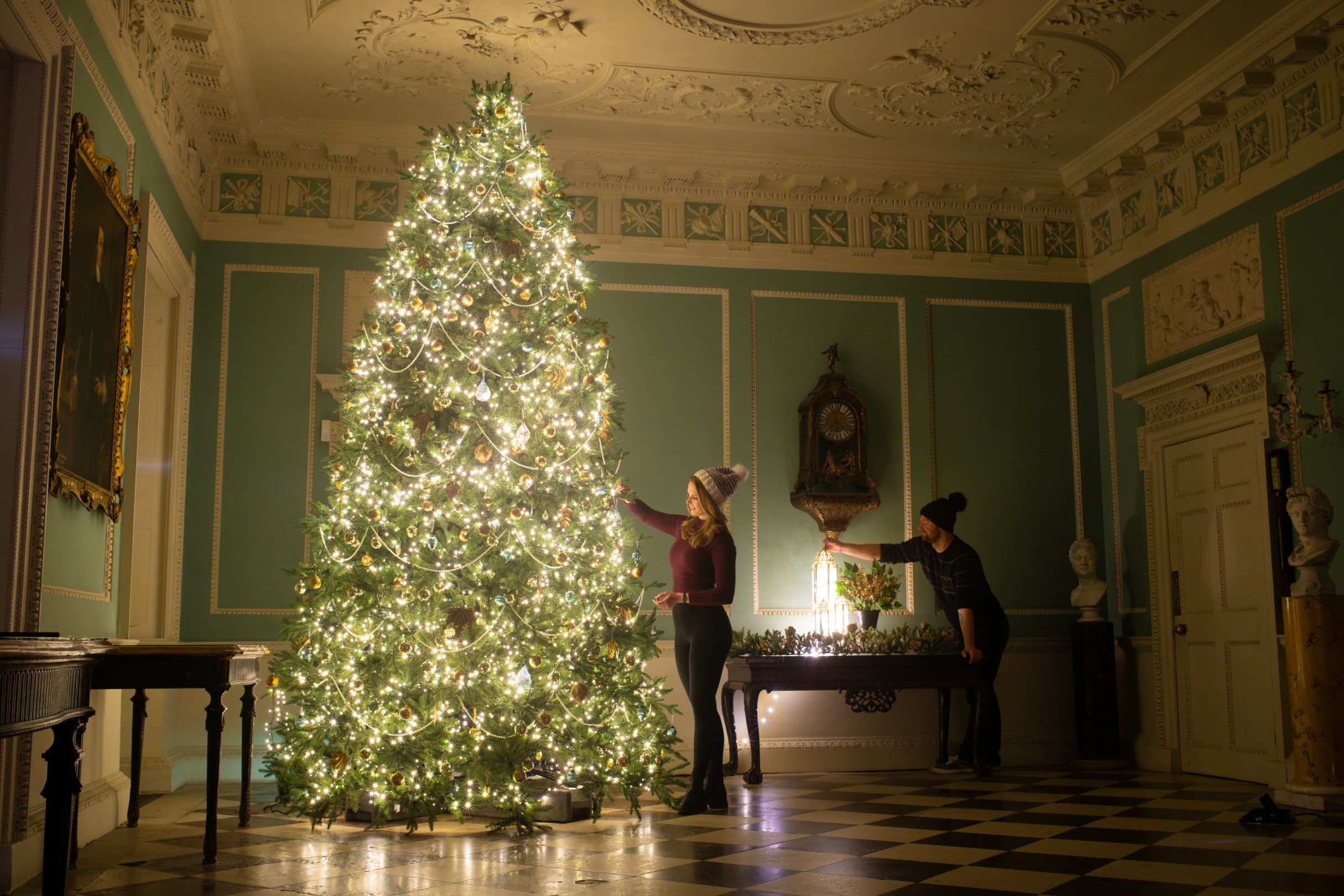 two staff members decorate the Entrance Hall Christmas tree at Saltram