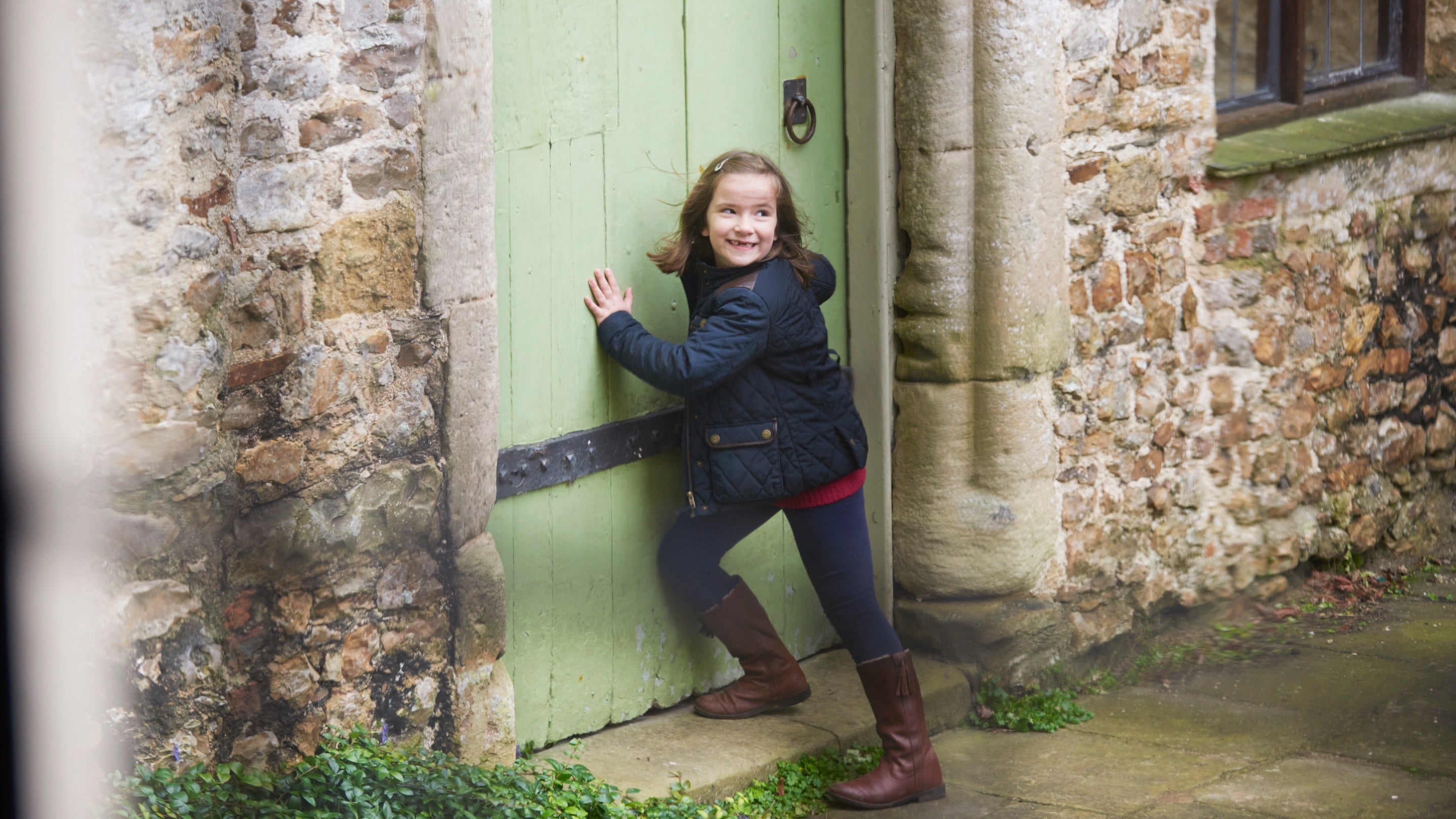 Child exploring a door in the courtyard at Shute Barton, Devon