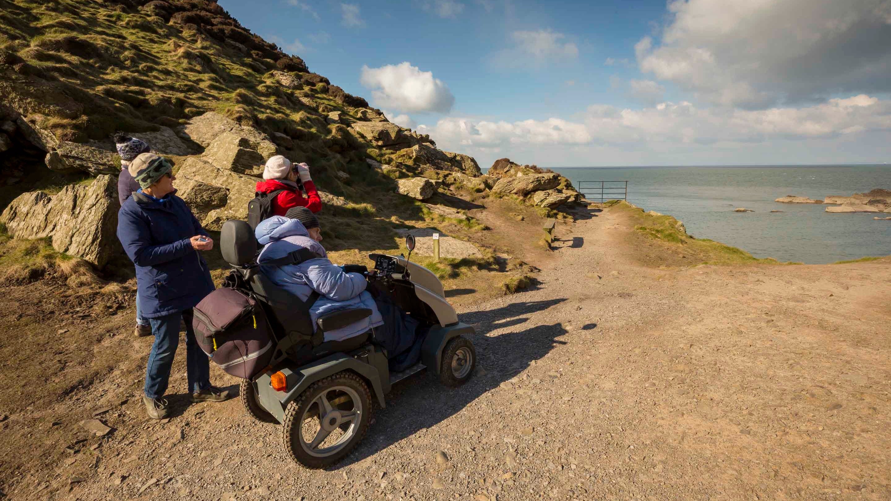 Four people, including one on a mobility scooter looking out to sea at Woolacombe