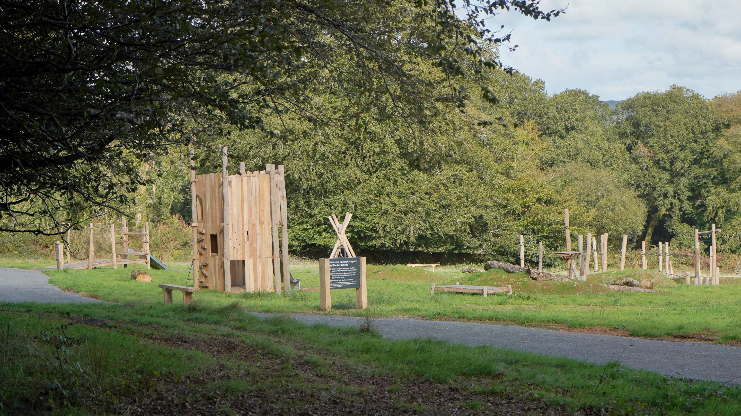 Looking out at play area which is lit by the sun in the distance and shows a tower made out of woods and logs to climb on