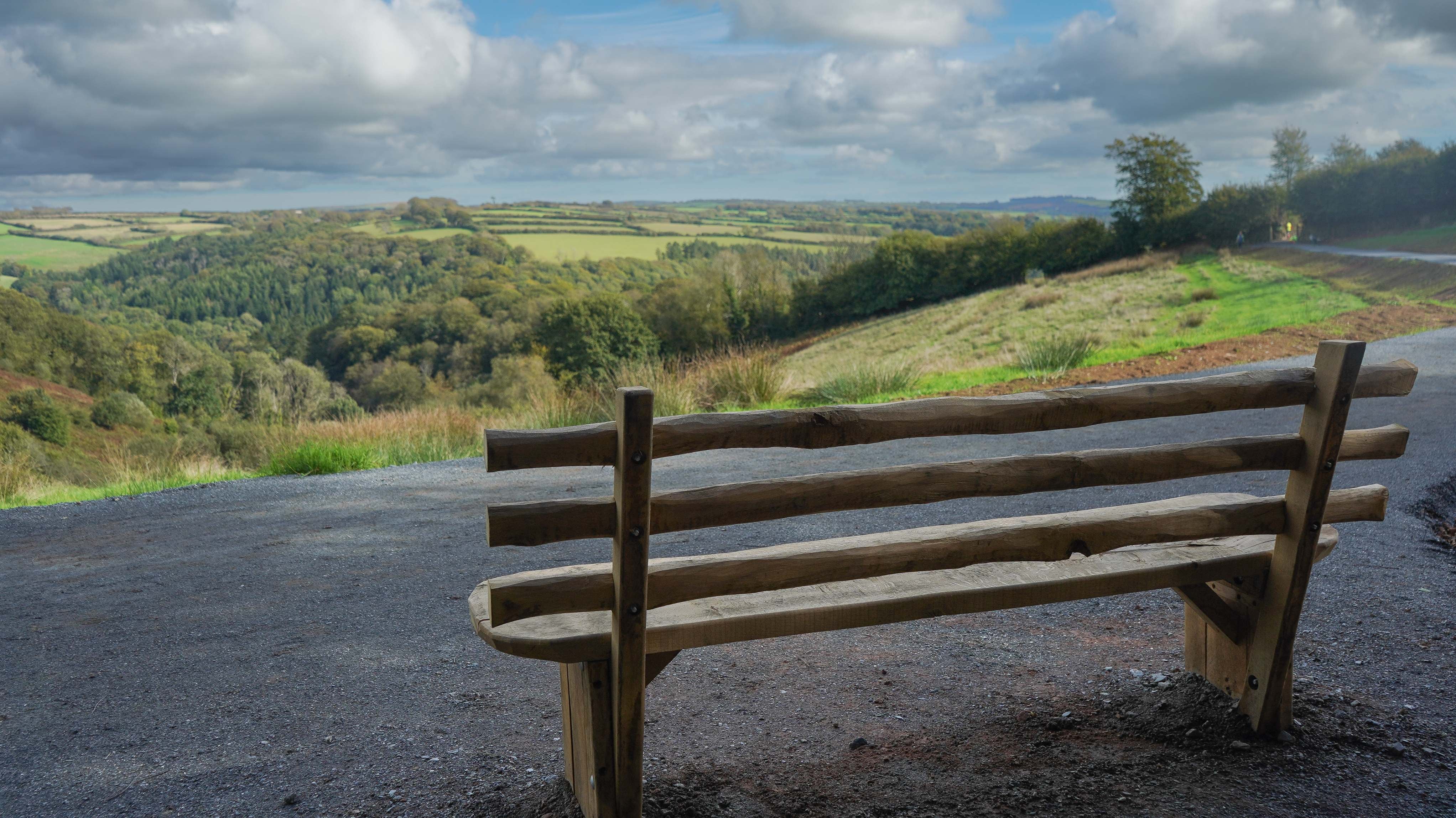 The back of a wooden bench looking out over views of a valley with rolling hills