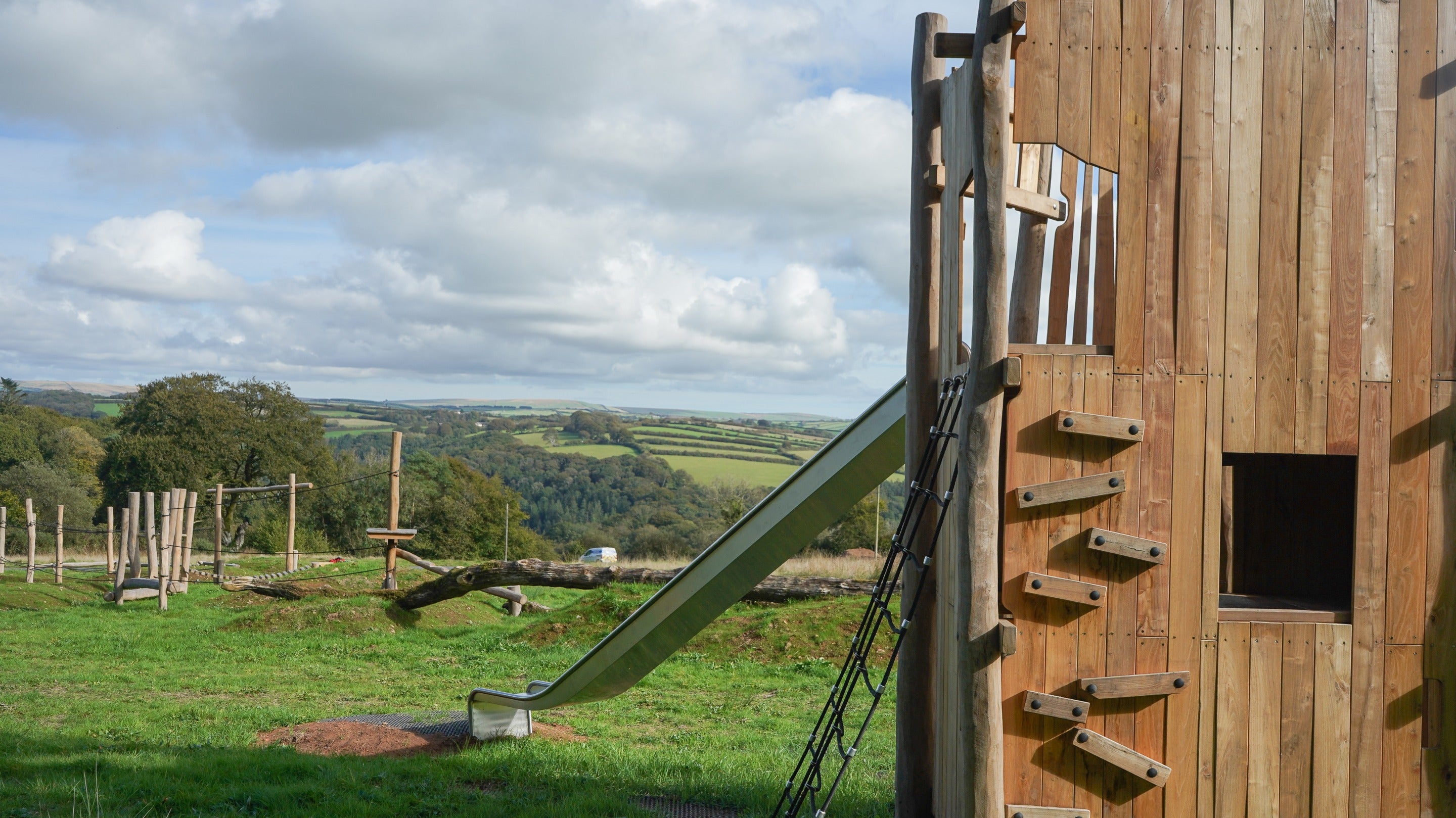 A wooden tower with a slide and wooden climbing equipment in the background