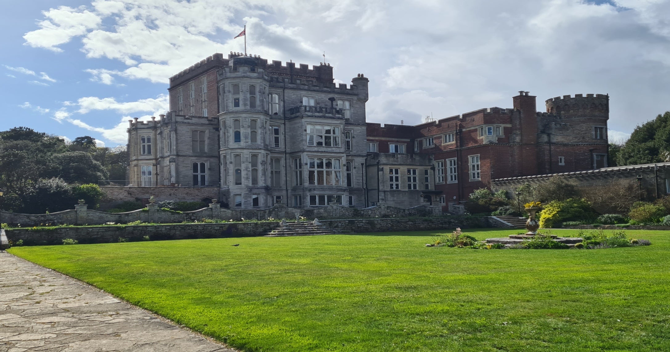 View of Brownsea Castle with a large lawn to the front and blue skies above.