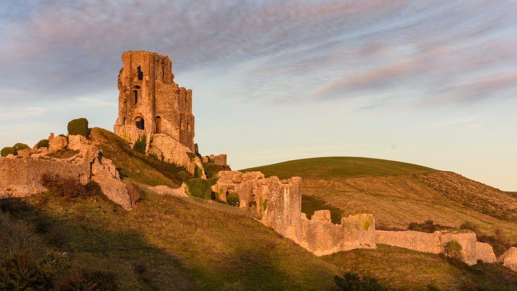 View of the ruins of Corfe Castle, lit in golden autumn sunlight, with a hill in the background