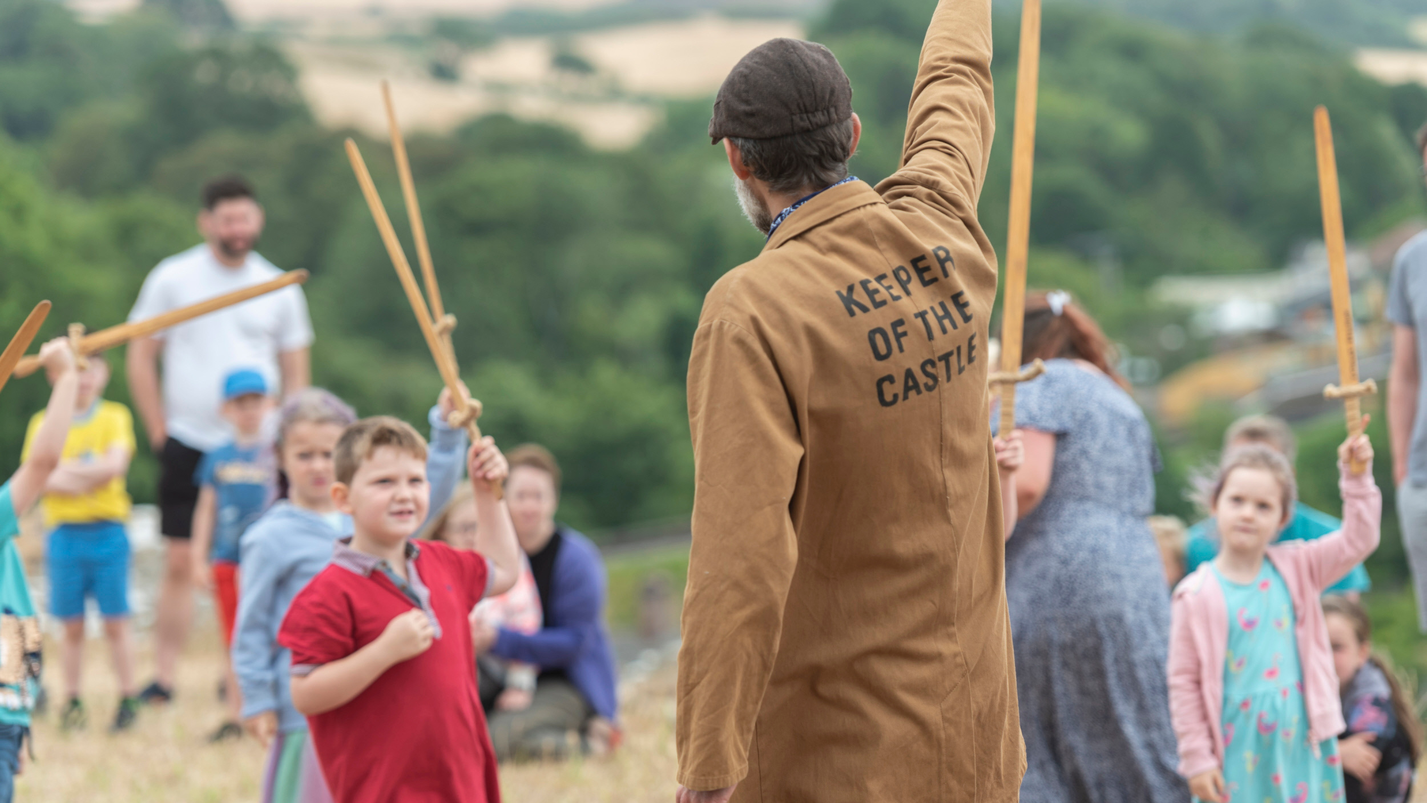 Picture of the Keeper of the Castle entertaining children on an interactive storytelling tour.  The children are gathered around the keeper and they're all holding up wooden poles.
