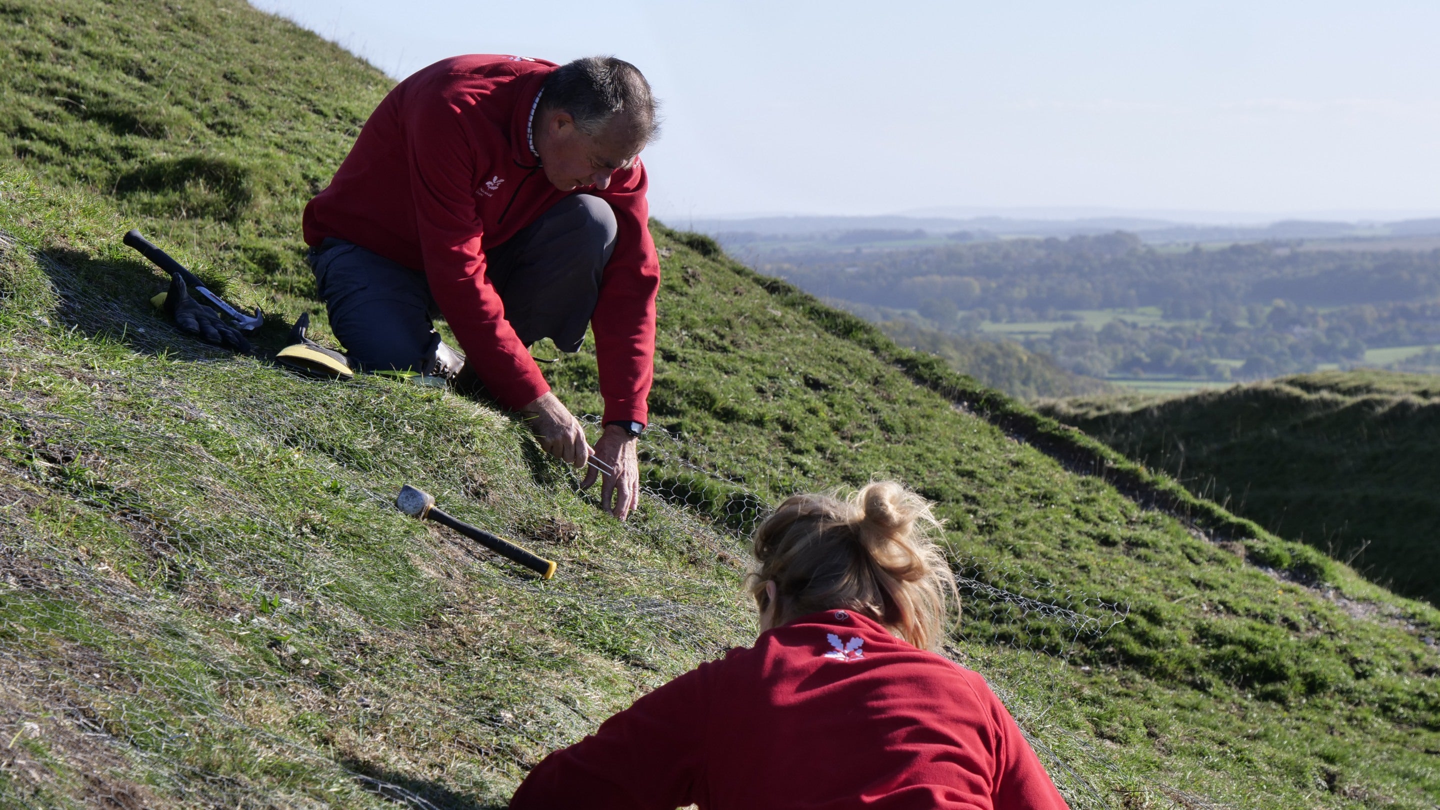Two volunteer rangers work on netting erosion repairs on the slopes of Hambledon Hill, Dorset
