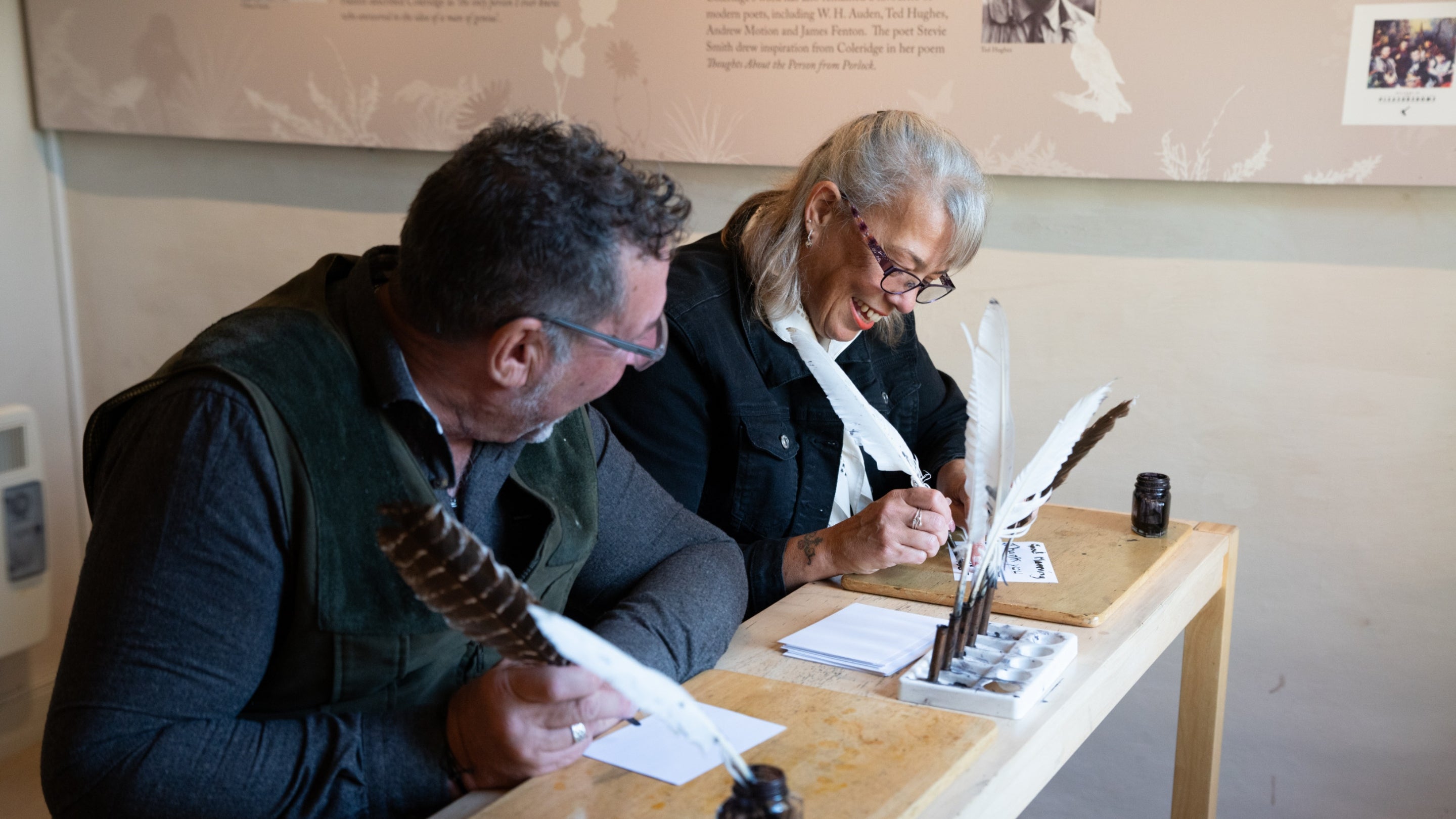 Two visitors have a go at writing with a quill and ink in the Interpretation Room at Coleridge Cottage, Somerset