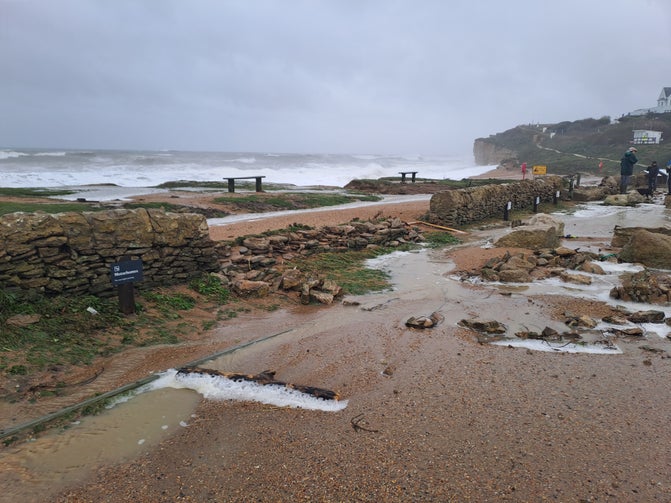 Walls broken by the force of a storm at Hive Beach, with debris into the car park and waves still significant in the background