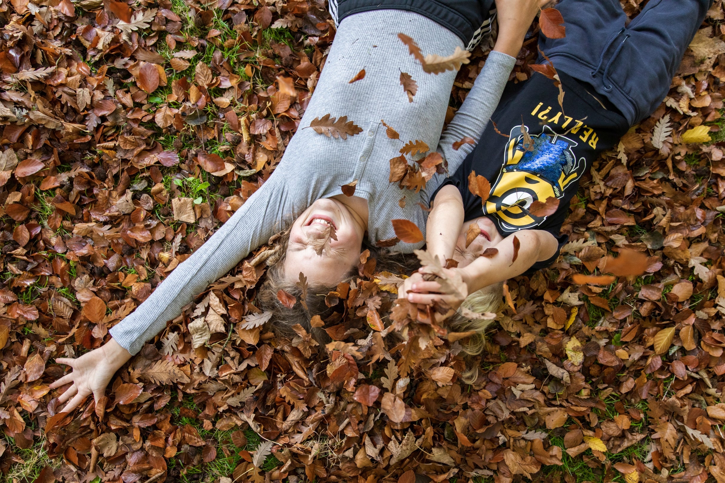 Two children laughing as they roll in dry oak leaves