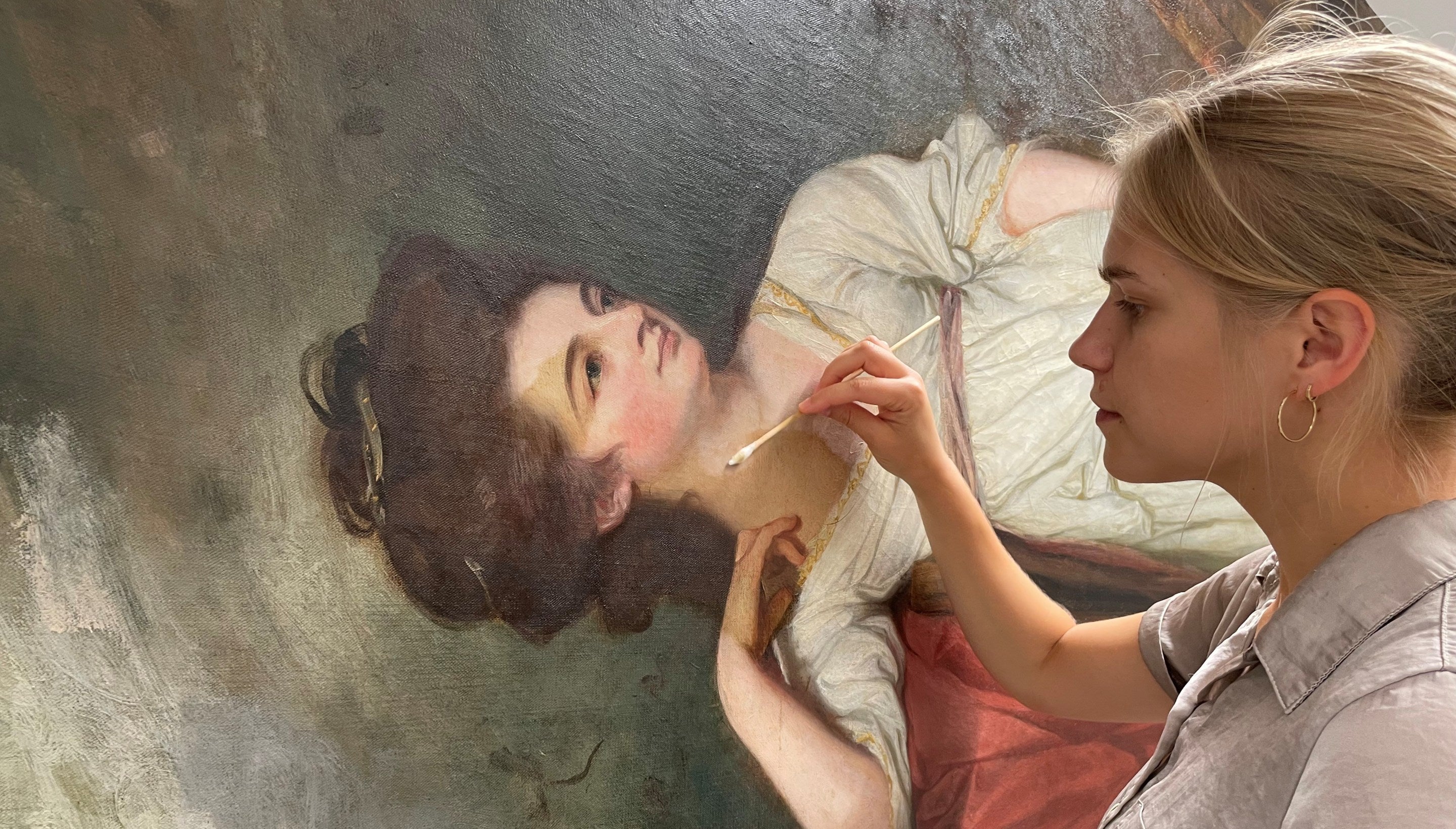 A woman using a swab to clean a portrait of an 18th century woman