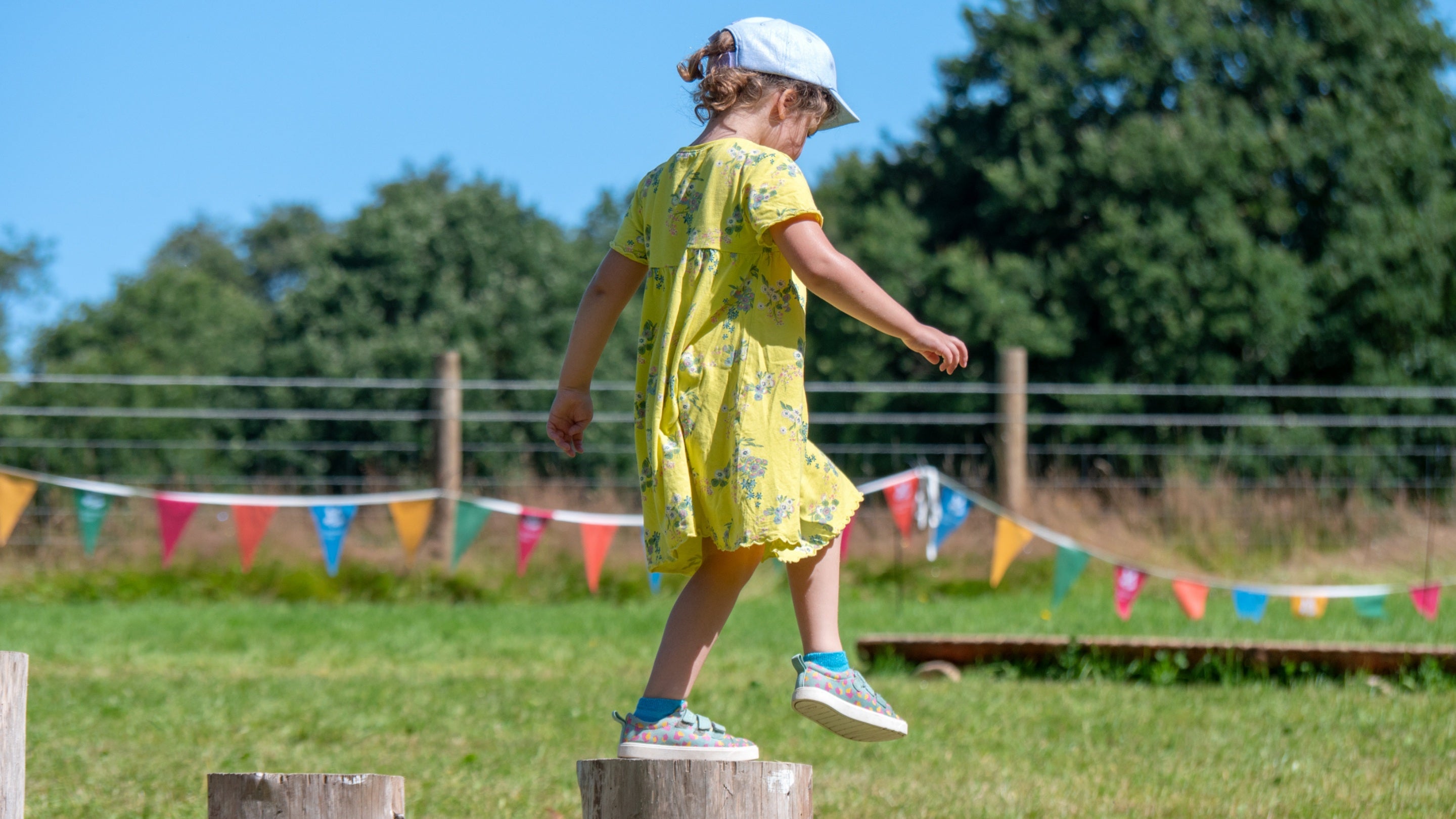 A child in a yellow summer dress playing on wooden stepping stones, with bunting behind