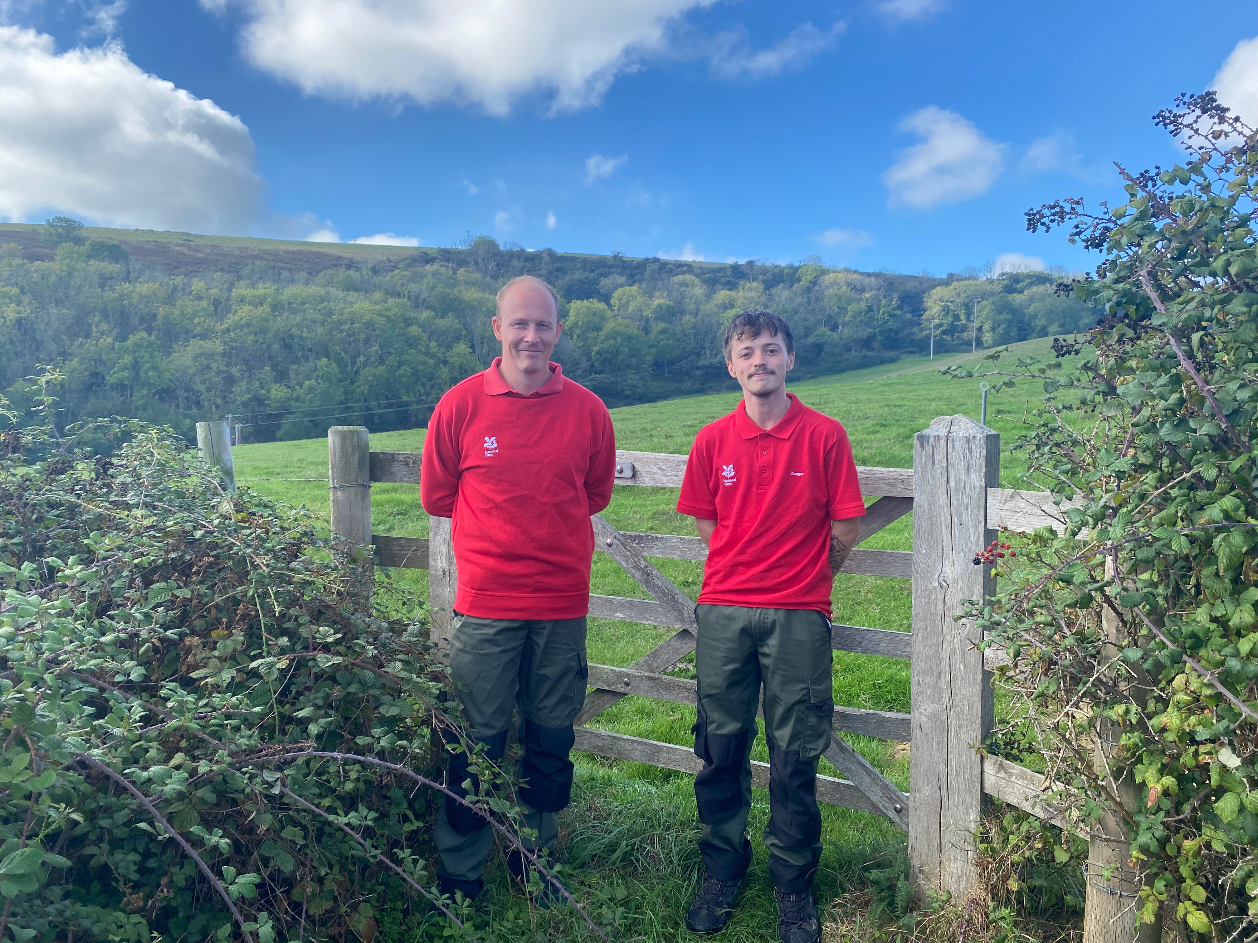Two rangers in red standing in front of a countryside gate.