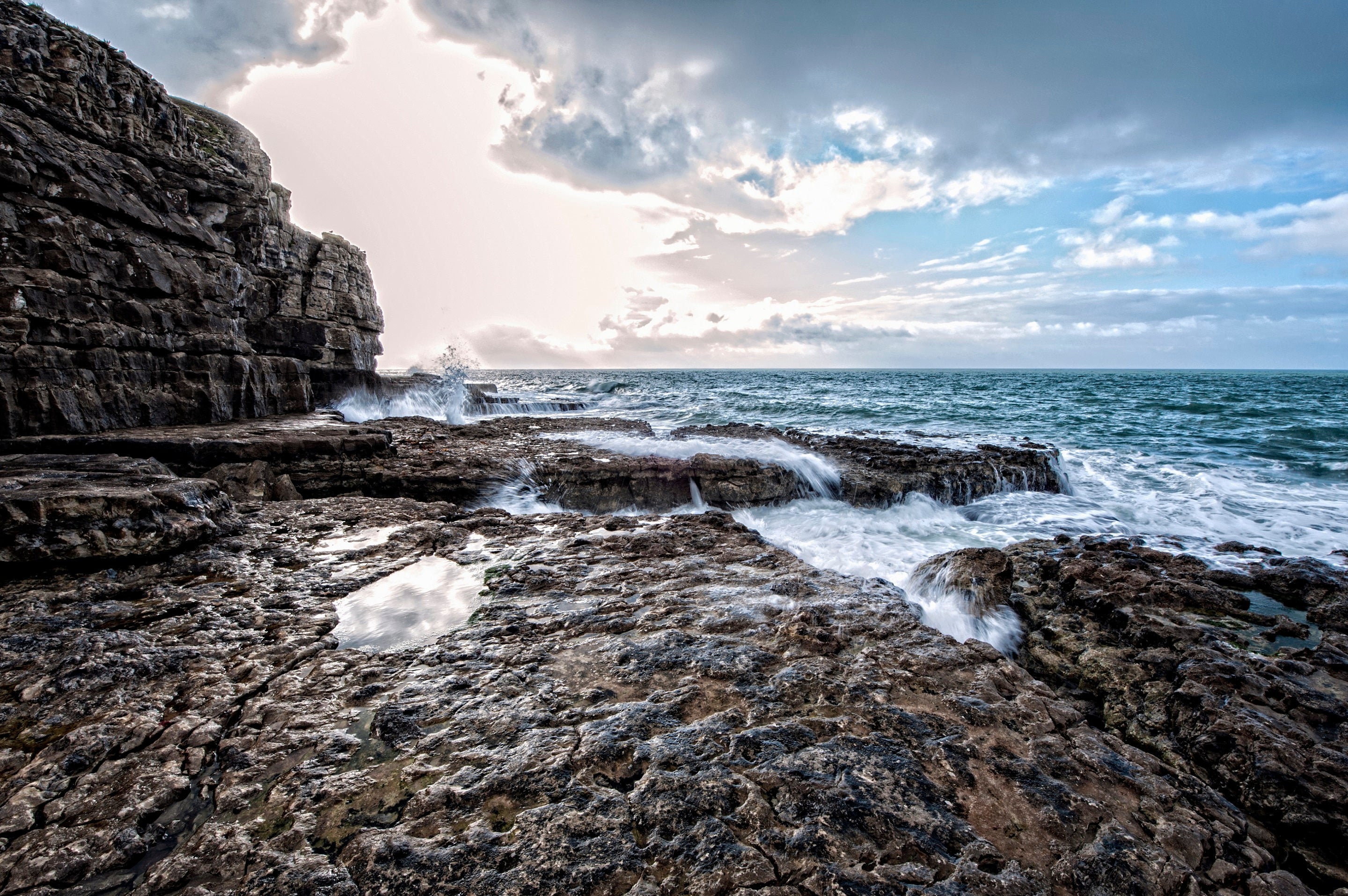 Waves crashing onto a rocky ledge, moody sunrise sky