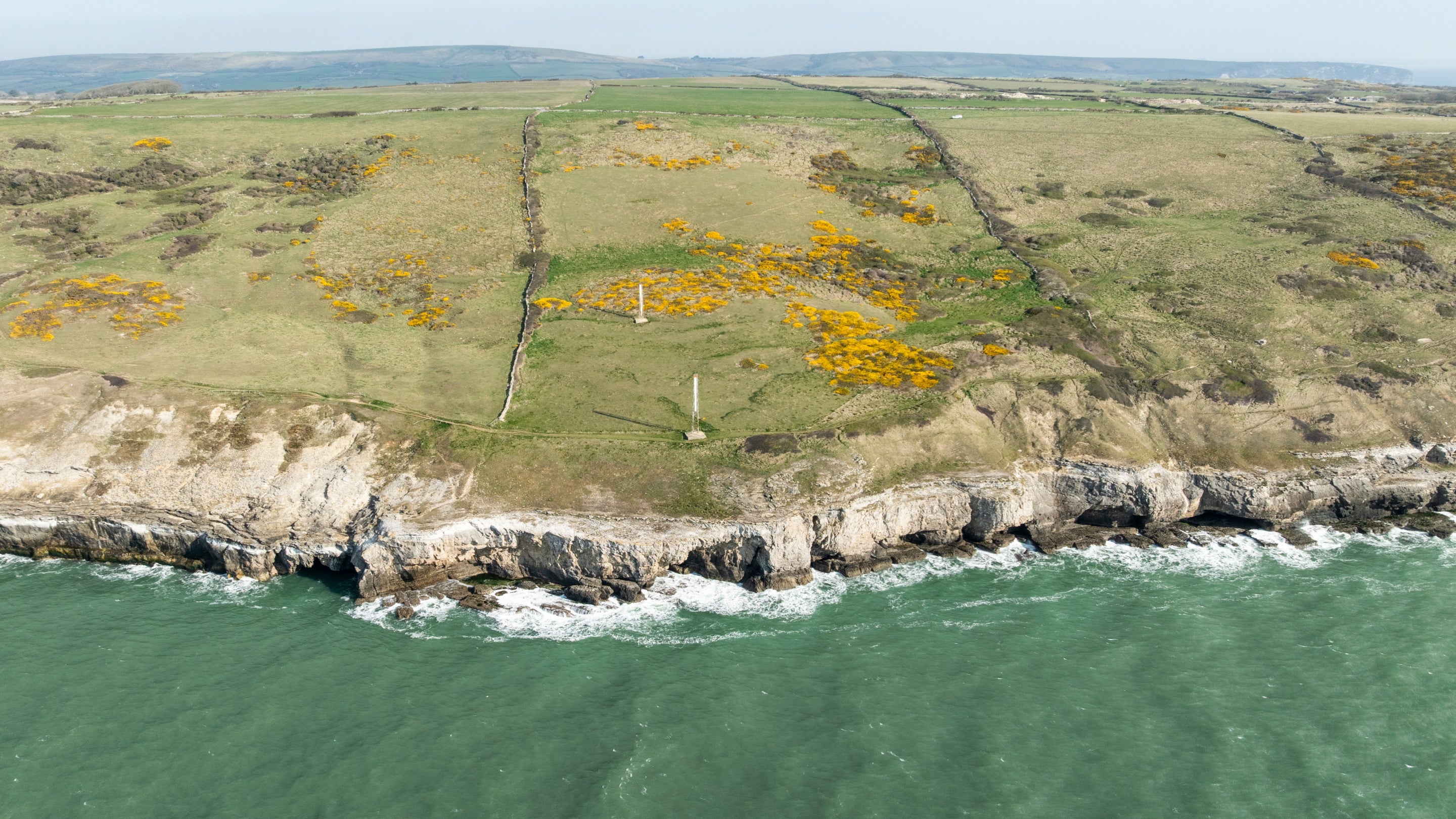 Aerial view of coastline showing the sea, steep cliffs and grassland beyond. The central section, defined by two stone walls, is the newly acquired land.