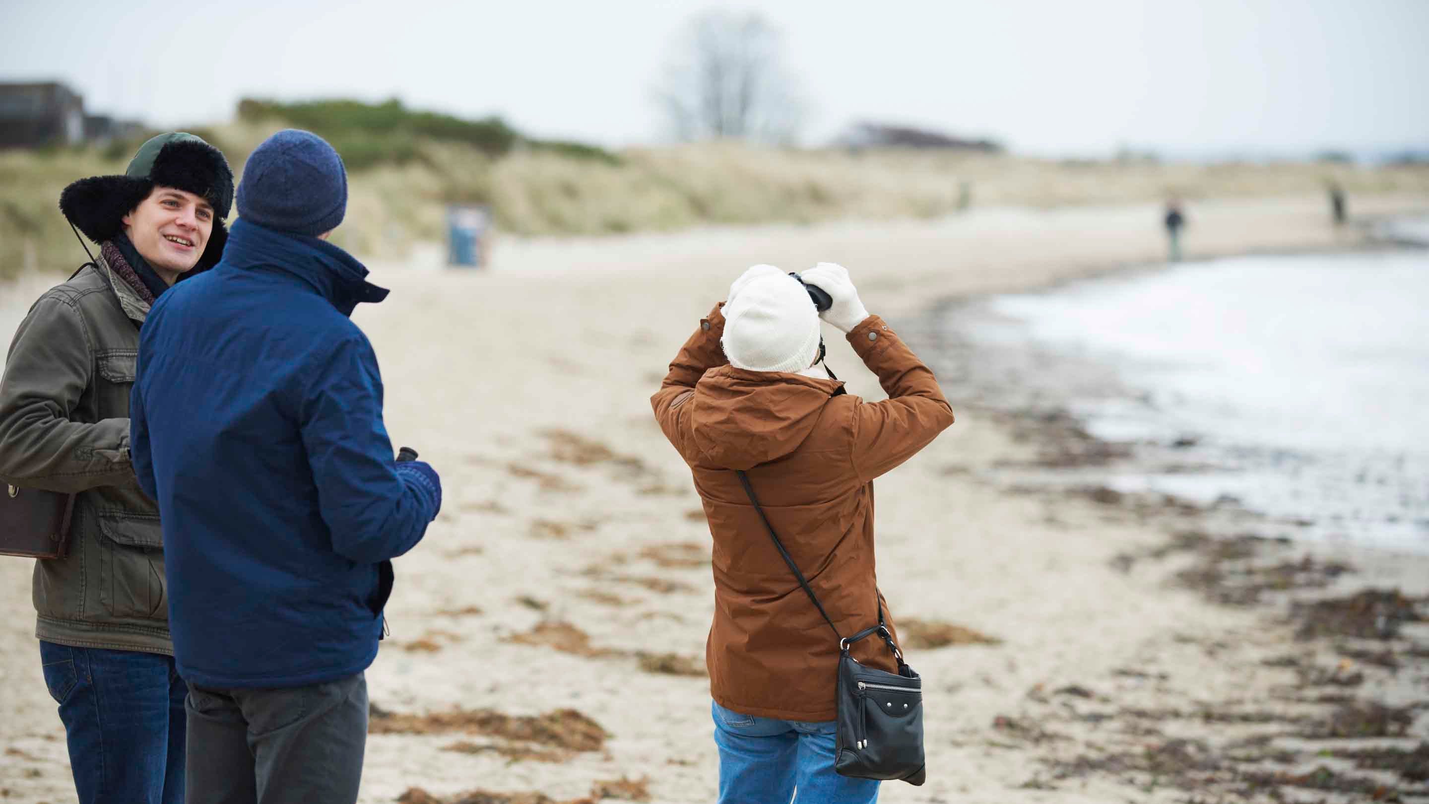 Three visitors birdwatching on the sand at Knoll Beach at Studland Bay, Dorset