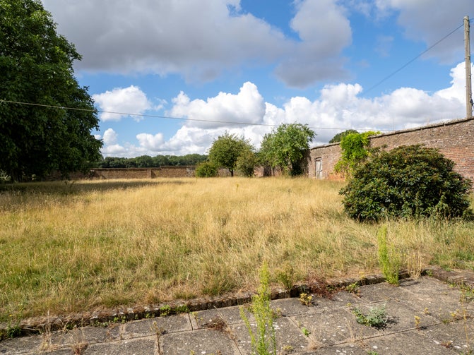 The current walled garden at Ward's Hurst Farm showing long grass, historic wall and mature trees