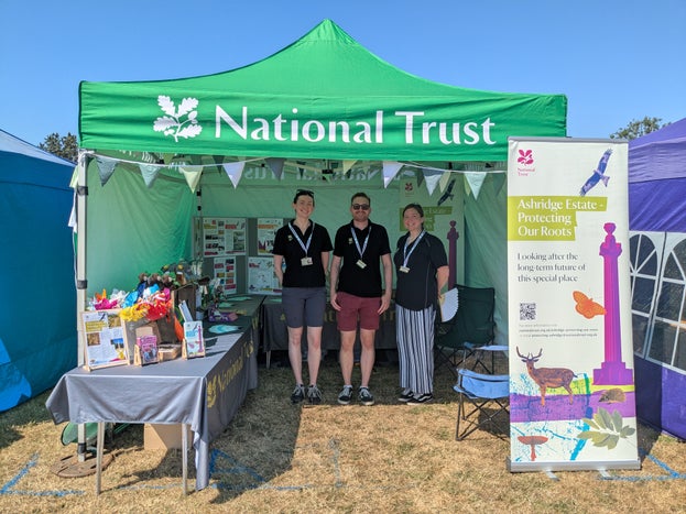 Three people wearing NT clothing standing in a green National Trust gazebo with banners and information leaflets
