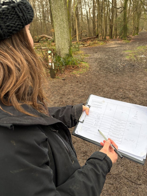 A woman holding a pad of paper and pen looking out at a muddy path
