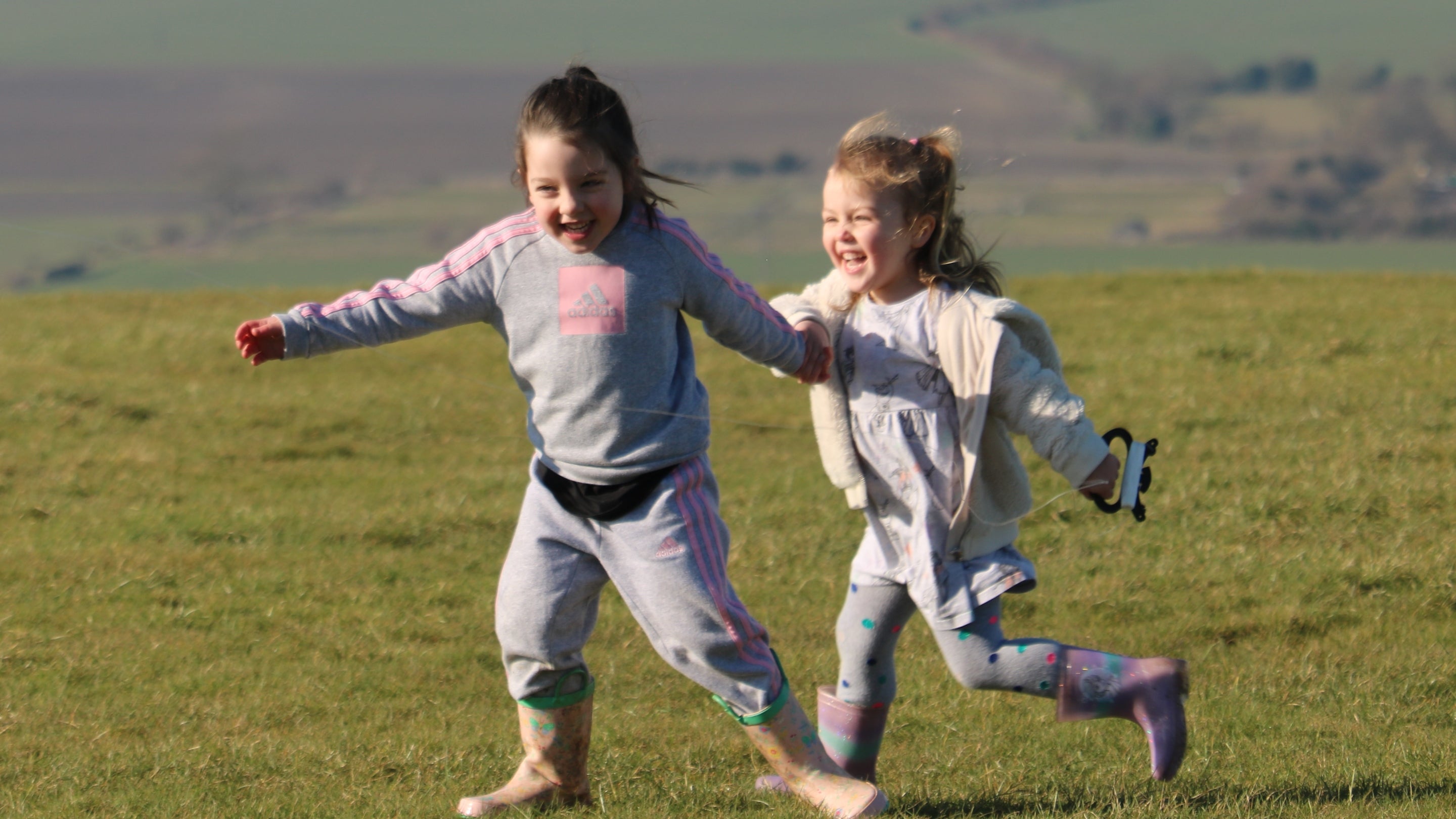 two young girls running on a field in wellies.