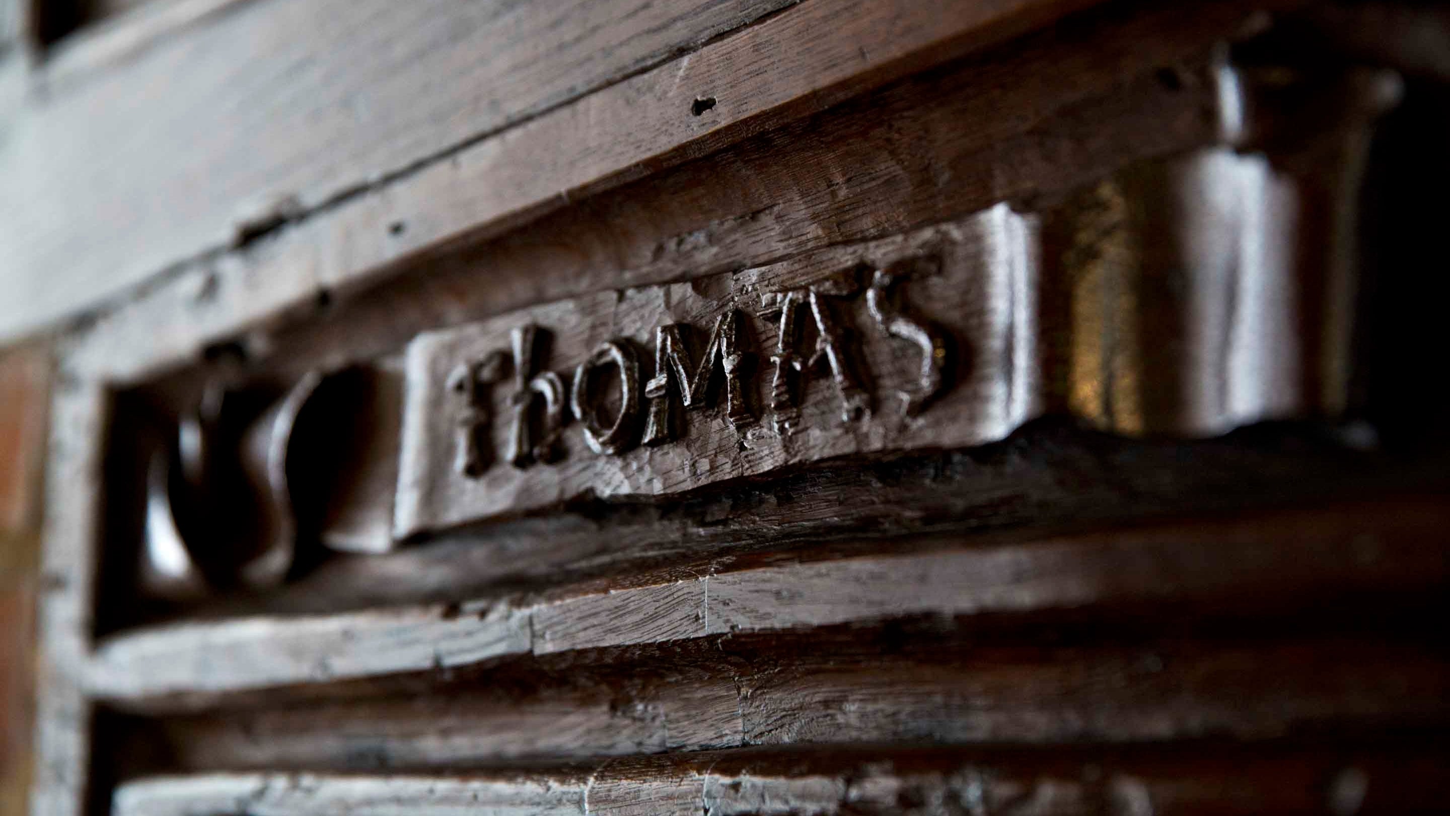 Detail of a wooden door plaque reading the name Thomas at Paycocke's House, Essex