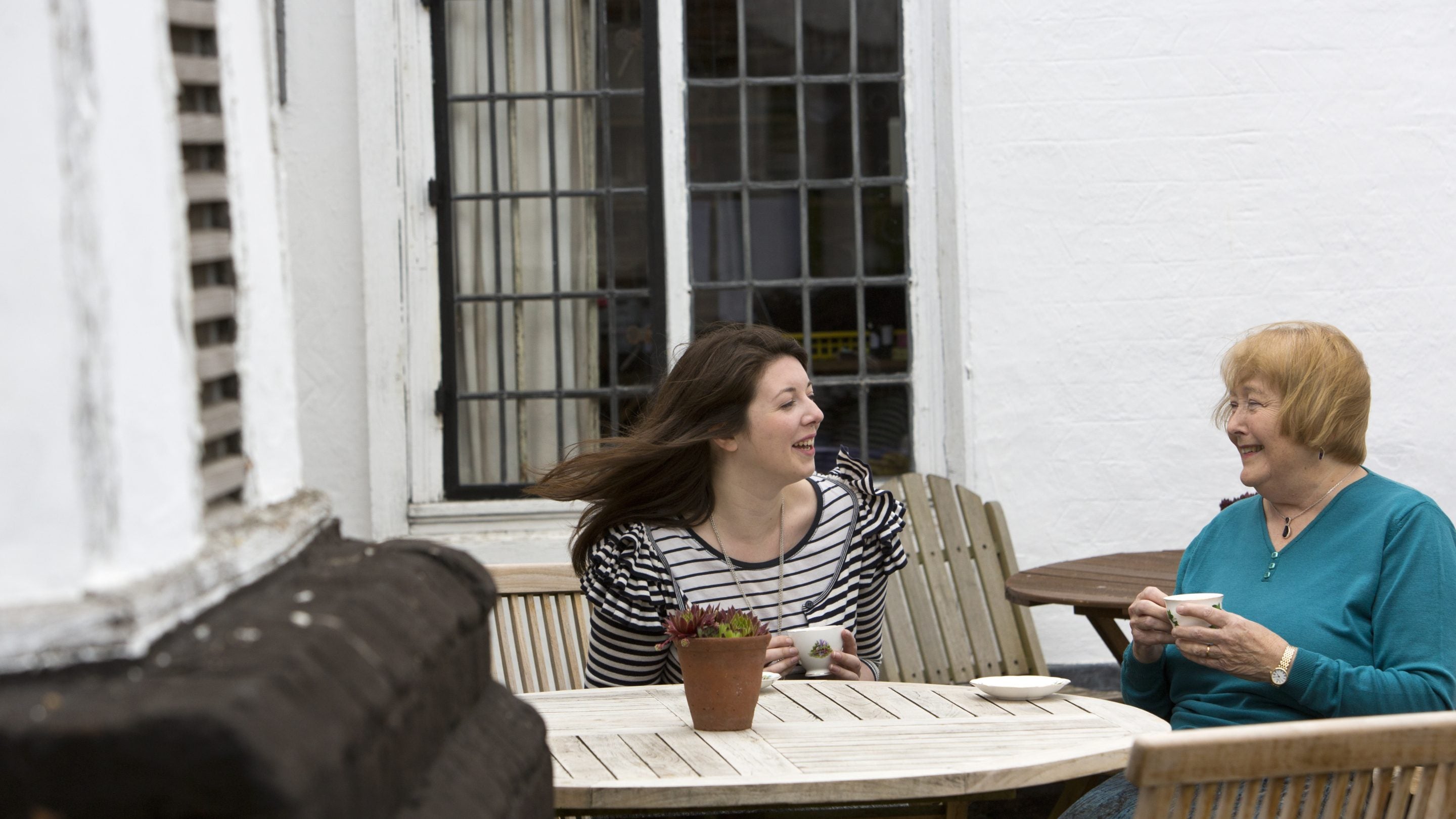 Two female visitors drinking cups of tea in the outdoor seating area of the tea room at Paycocke's House and Gardens, Essex