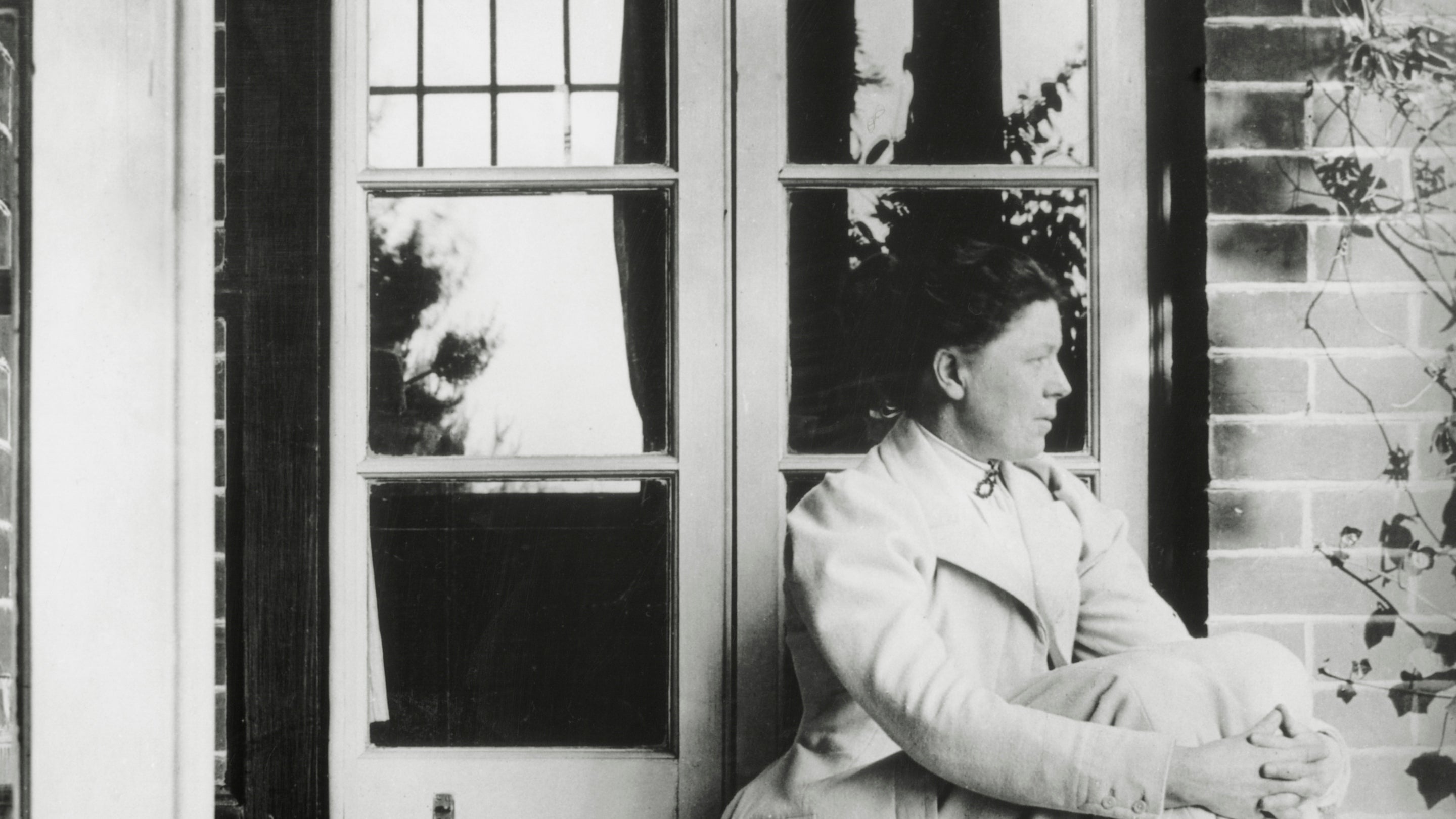 Black and white archive photo of Charlotte Shaw sitting on a step outside a french window at Shaw's Corner, Hertfordshire